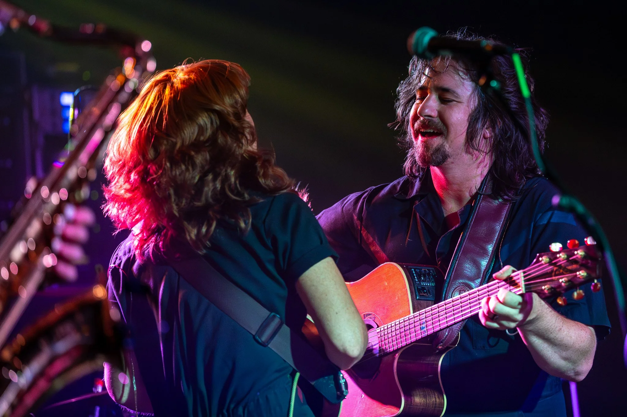 Two musicians performing on stage, playing guitars and singing with vibrant lighting effects.