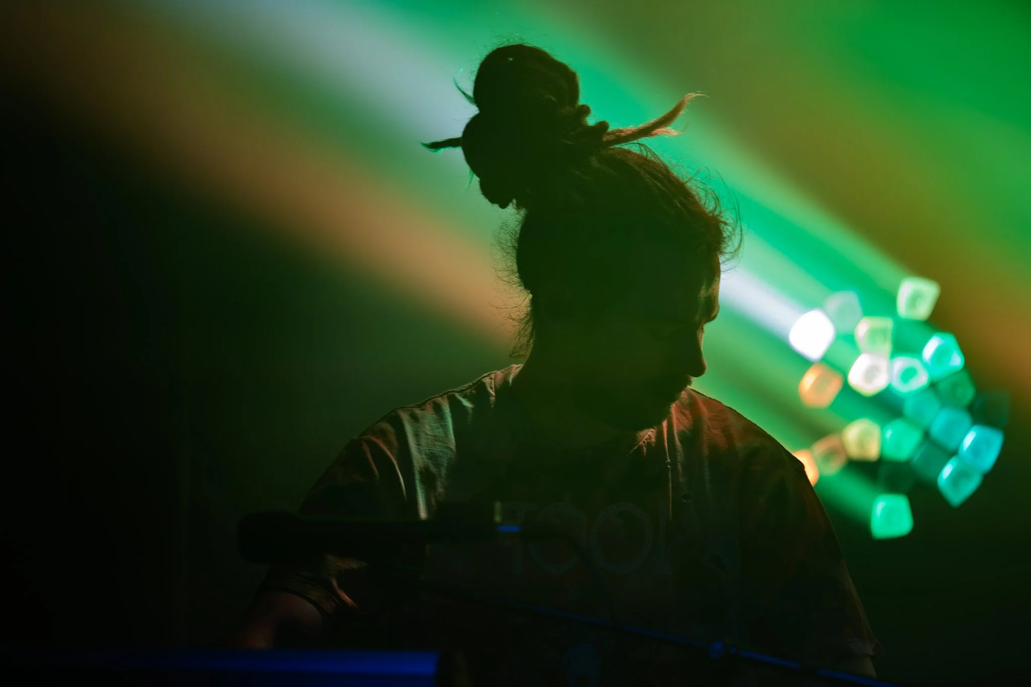 Silhouette of a person with dreadlocks in a dark setting with colorful lights in the background.