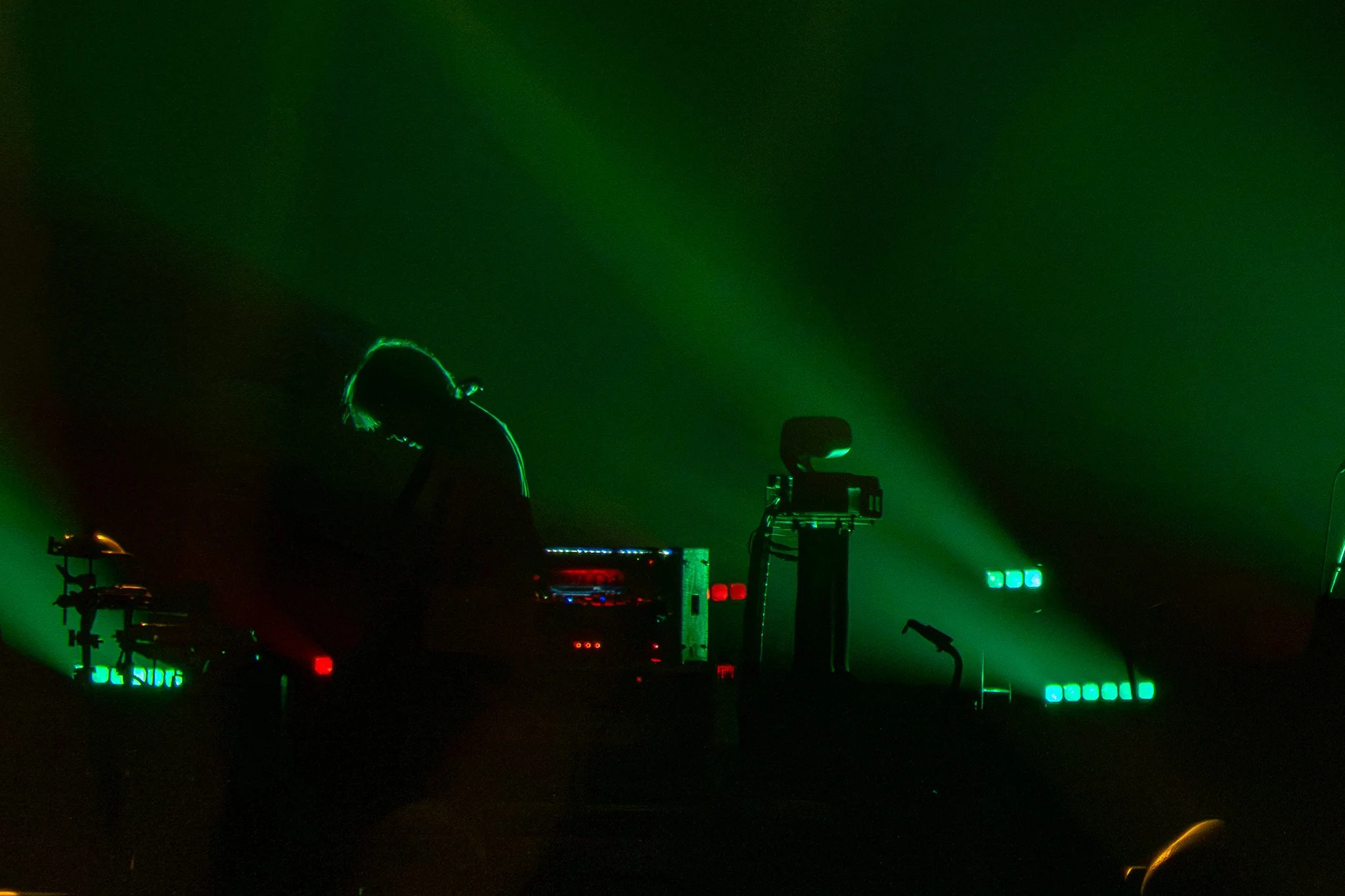 Dark scene with silhouettes of DJ equipment and green laser lights creating abstract patterns.