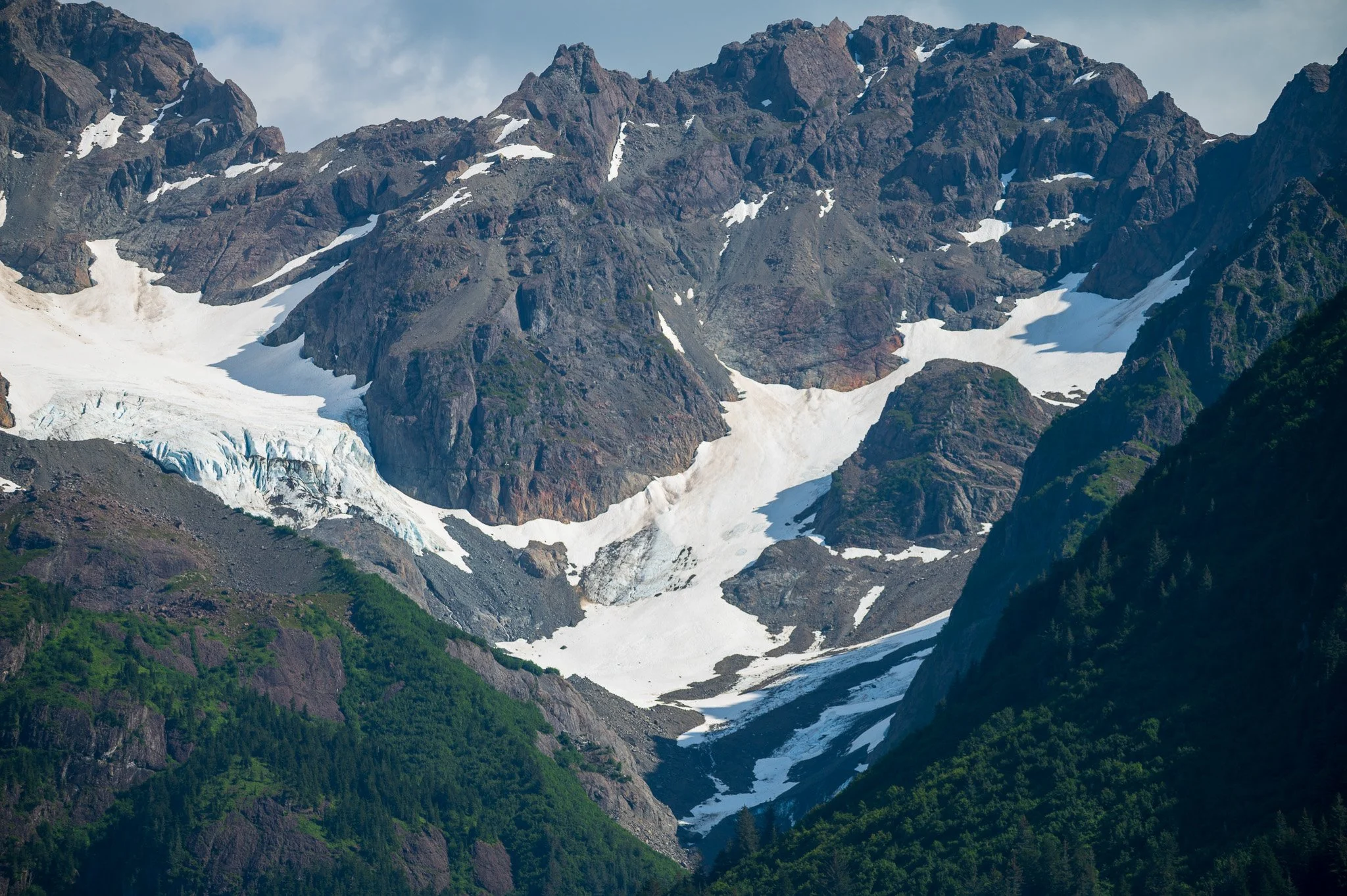 Snow-capped mountains with rocky peaks and green forested slopes.