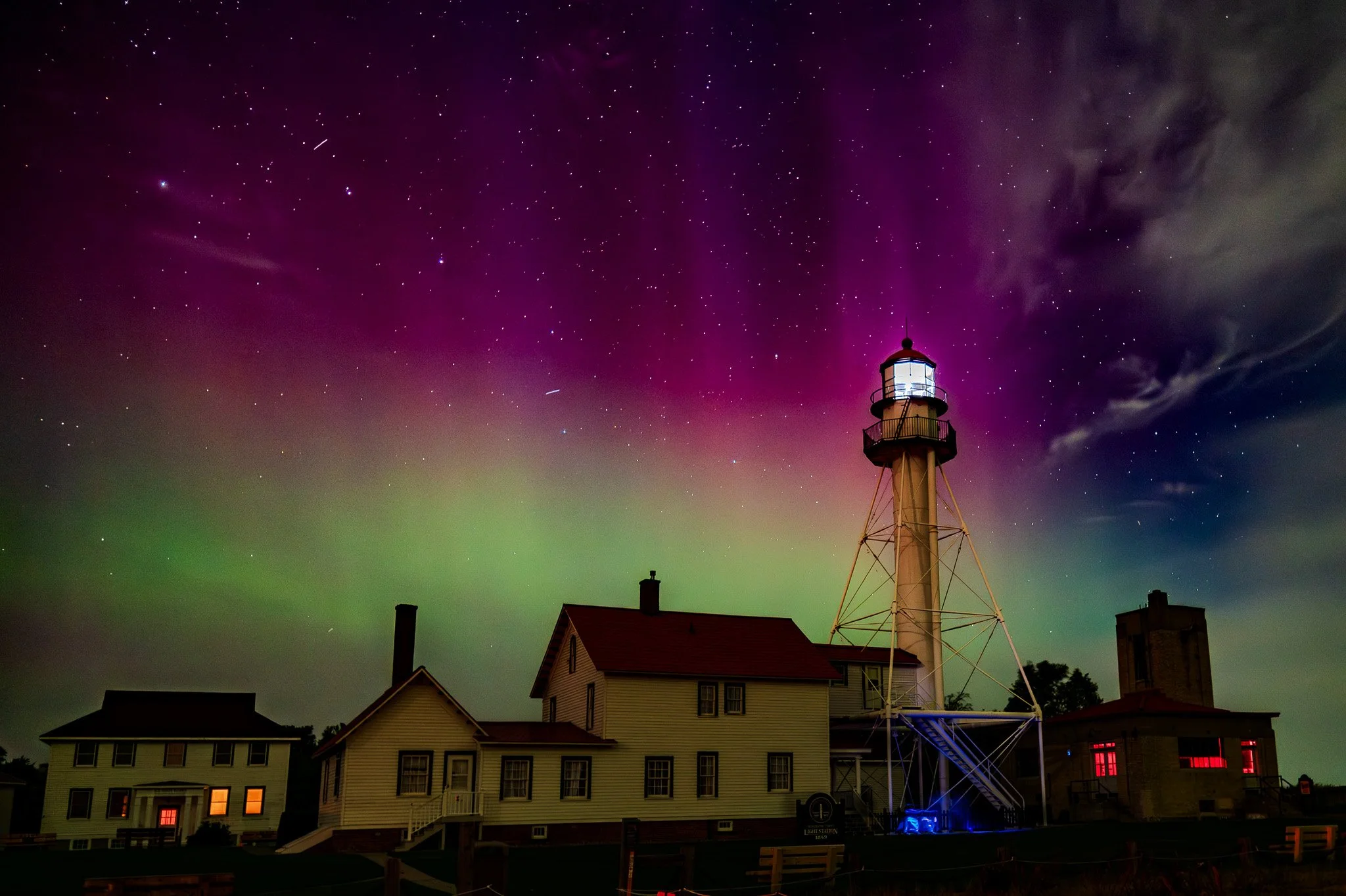 Night sky with stars and the northern lights over a lighthouse and houses