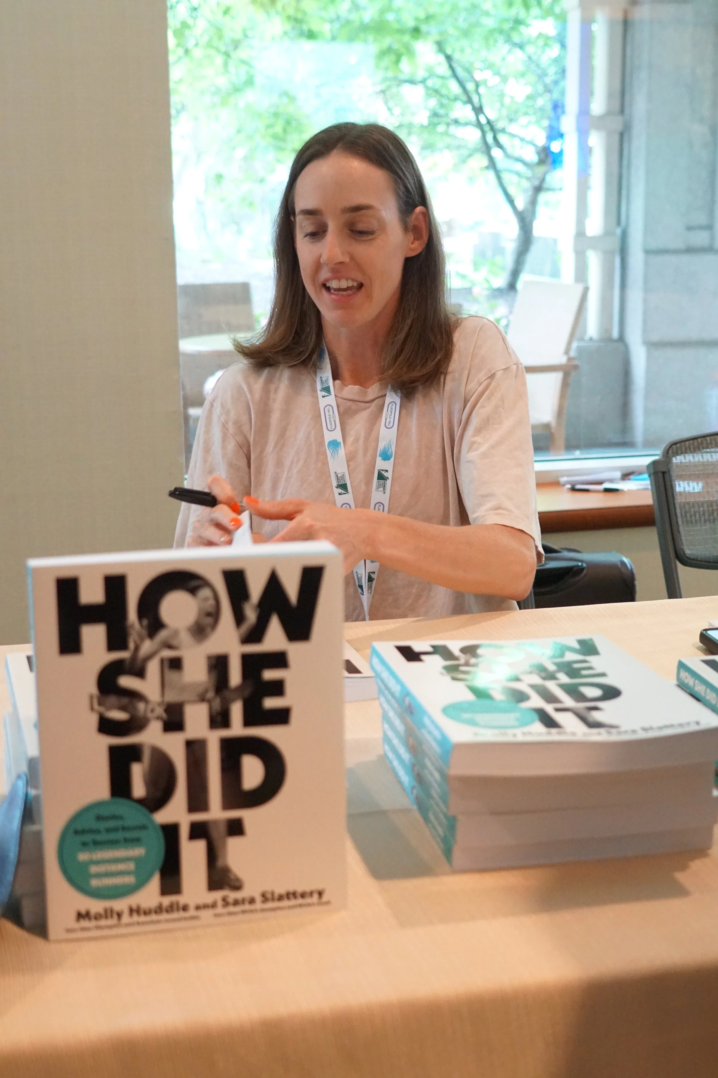 Book titled "How the Bird Got Its Beak" by Melly Nedder and Sara Slattery on a table with several copies and a person sitting in the background.