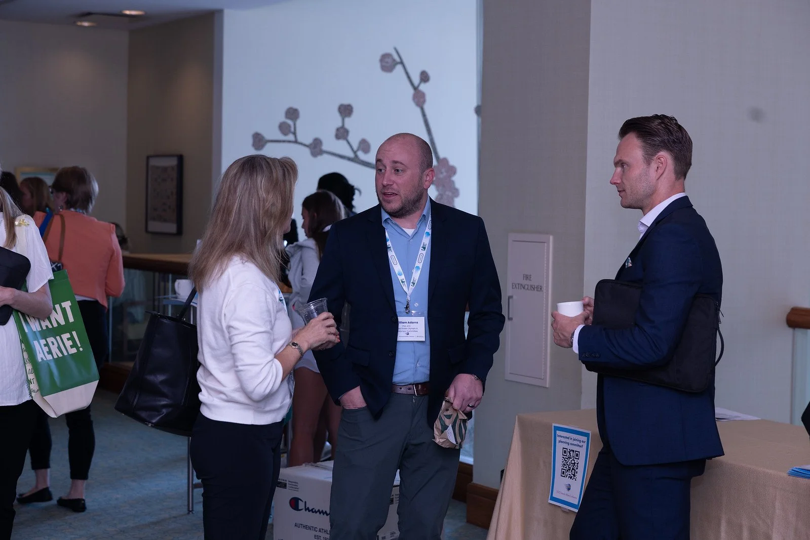 People at a professional conference engaging in conversation near exhibitor booths, with some holding cups and informational materials.