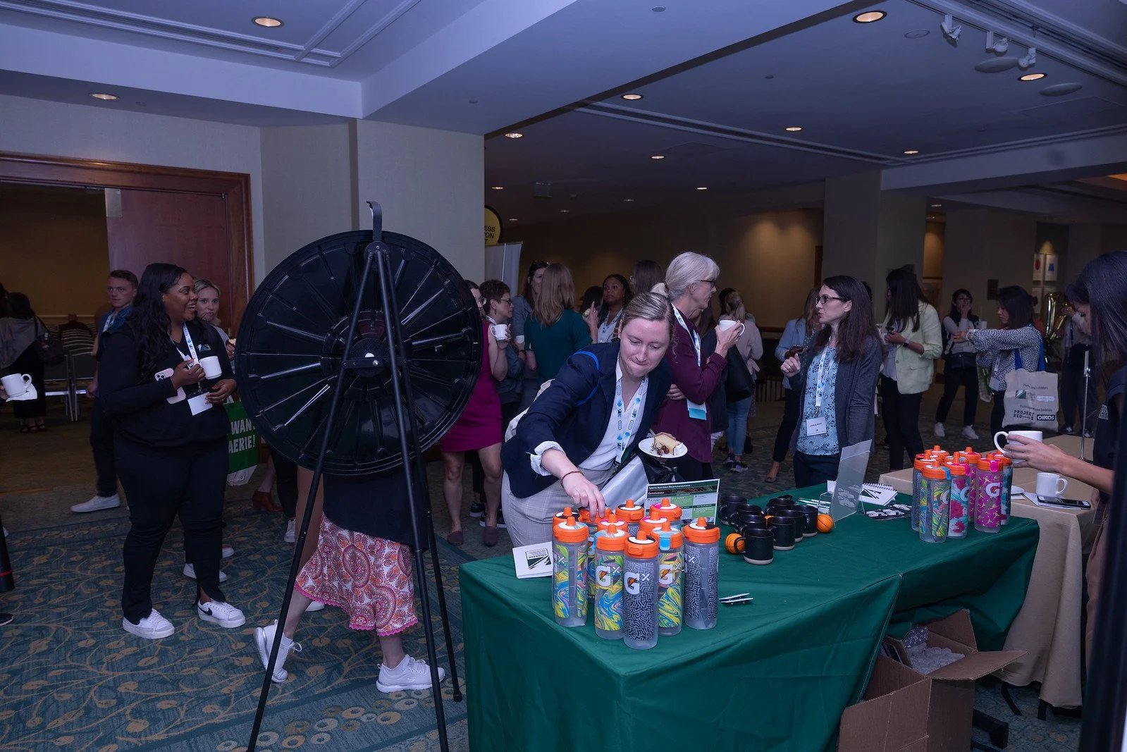 Conference or event attendees gathered around a booth with Gatorade water bottles and cups, some engaged in conversation, and a woman reaching for a water bottle.