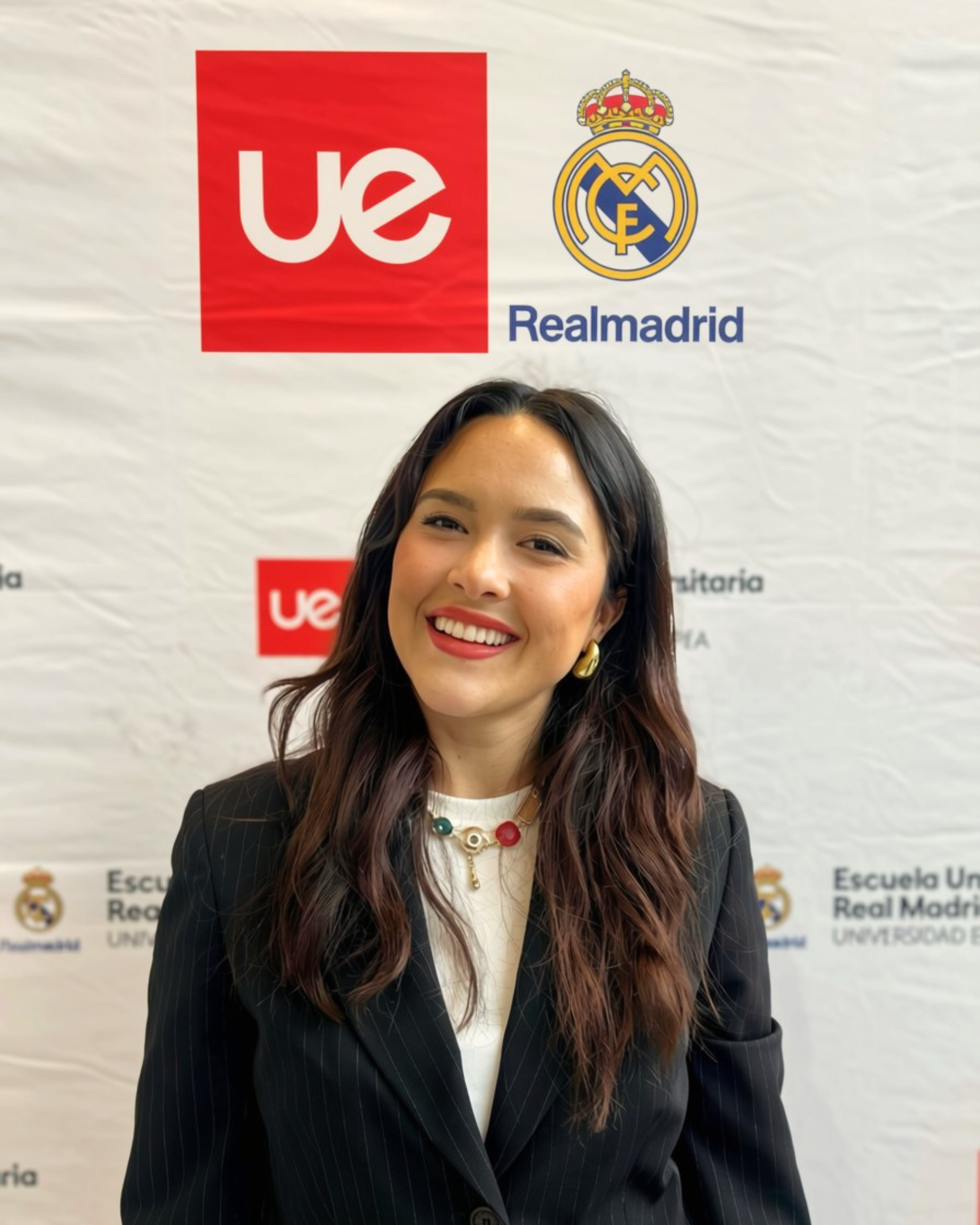 Ein Mann posiert vor einem Hintergrund mit den Logos von UE und Real Madrid in einer offiziellen Veranstaltung.