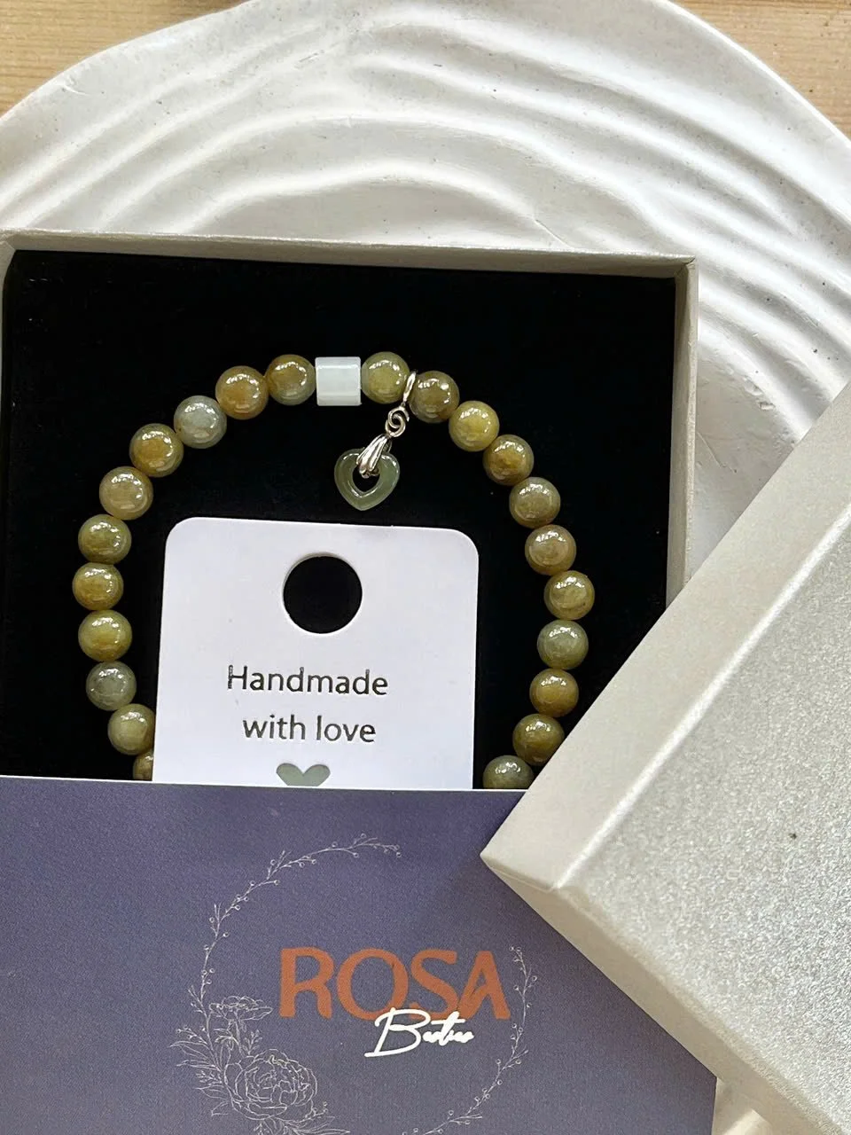 Beaded bracelet with a silver toggle clasp, displayed inside a white gift box with a card that says 'Handmade with love,' and a purple label with 'ROSA Boto' in orange and white text, and floral design.