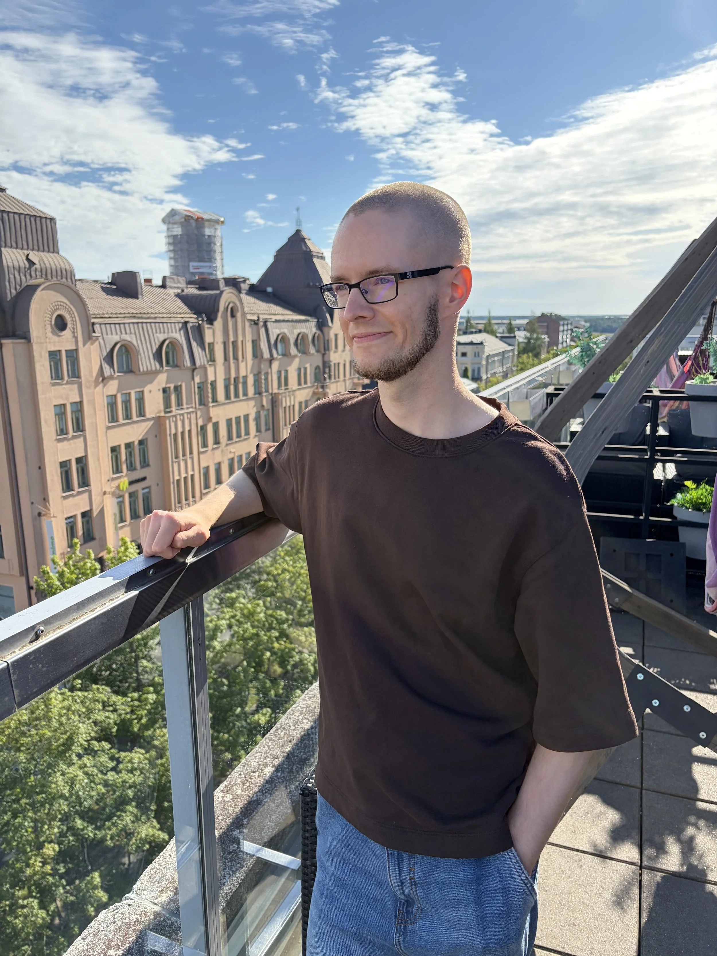 Antti Raatikainen seisoo terassilla rauhallisesti hymyillen ja katsoo kaupungin maisemaan.