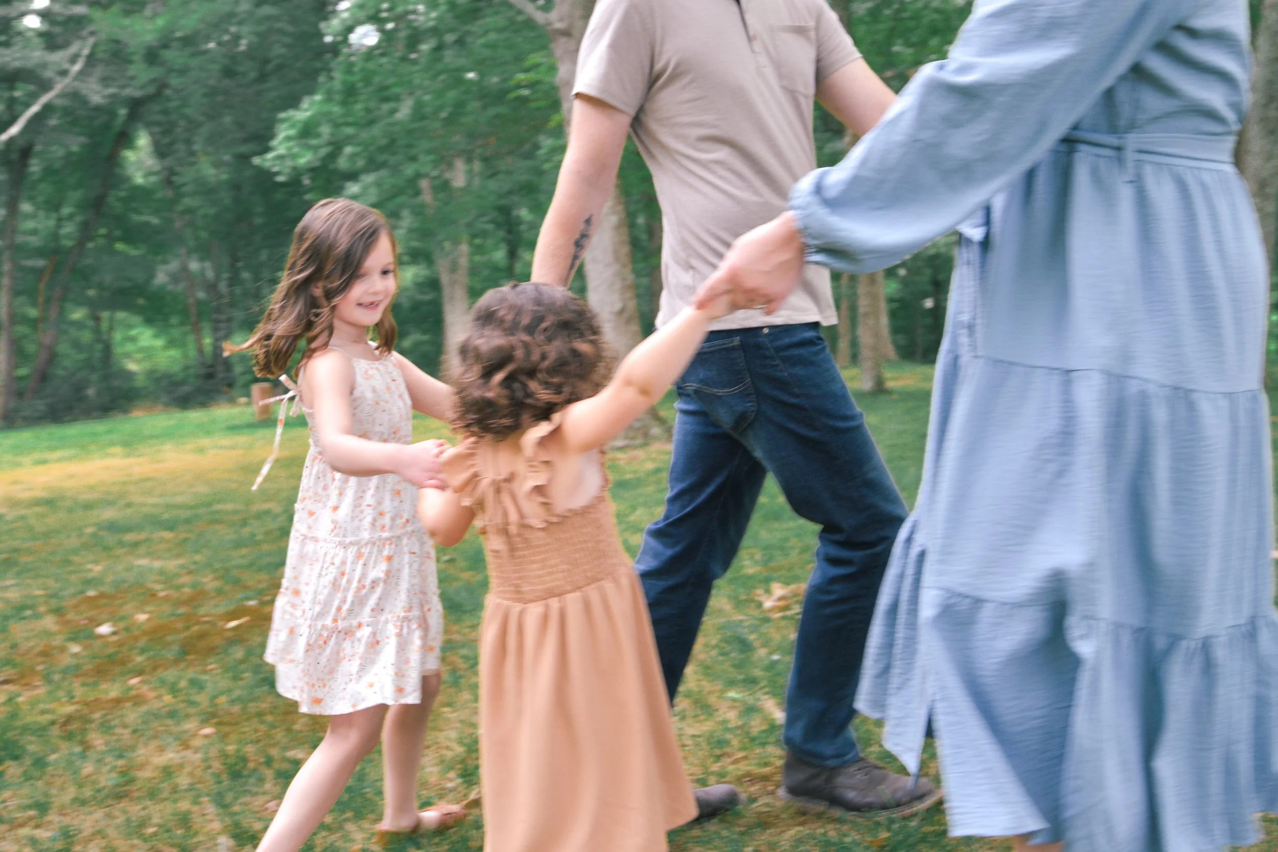 Children and adults holding hands and playing outdoors in a park with green grass and trees.