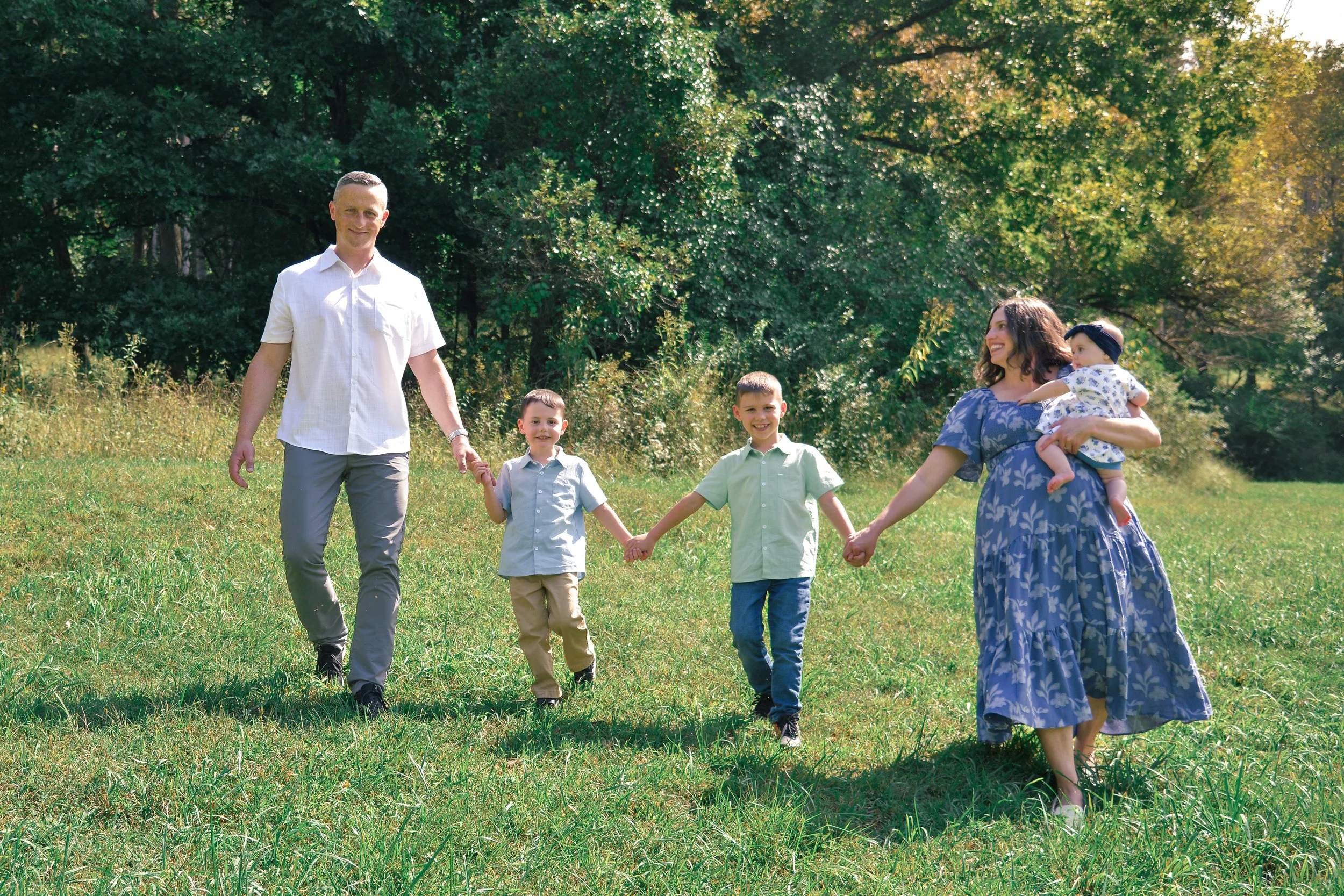 A family walking hand-in-hand on a grassy field in a forested area during daytime.