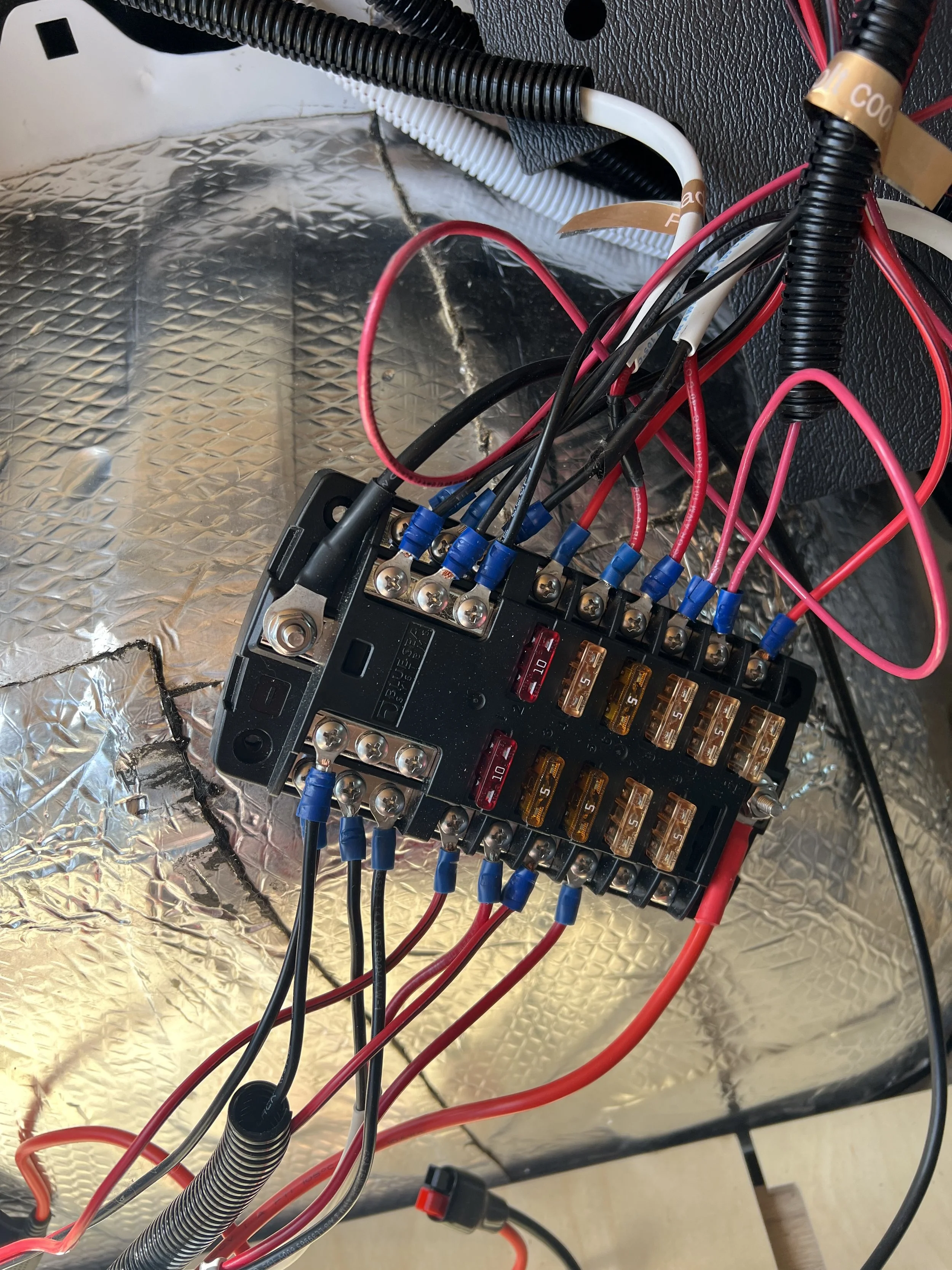 Close-up of an electrical circuit panel with multiple wires connected to a terminal block, with a reflective metallic surface underneath.