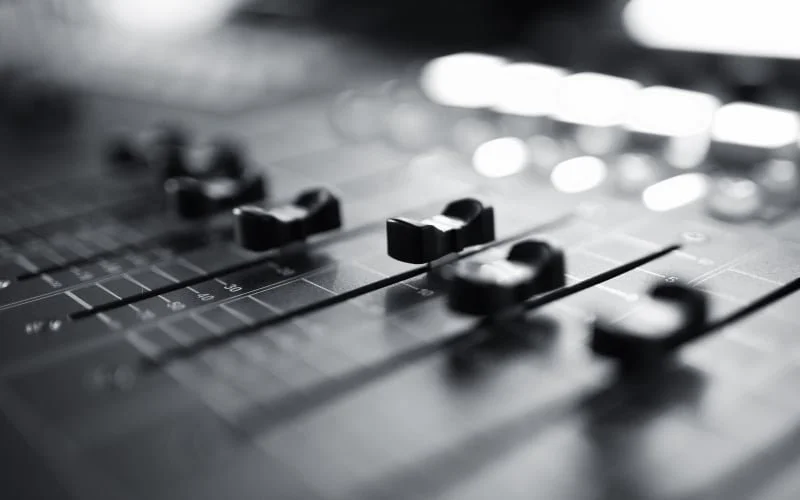 Close-up of a sound mixing board with sliders and knobs.