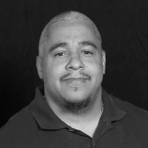 Black and white portrait of a smiling man with short hair and a goatee, wearing a collared shirt.