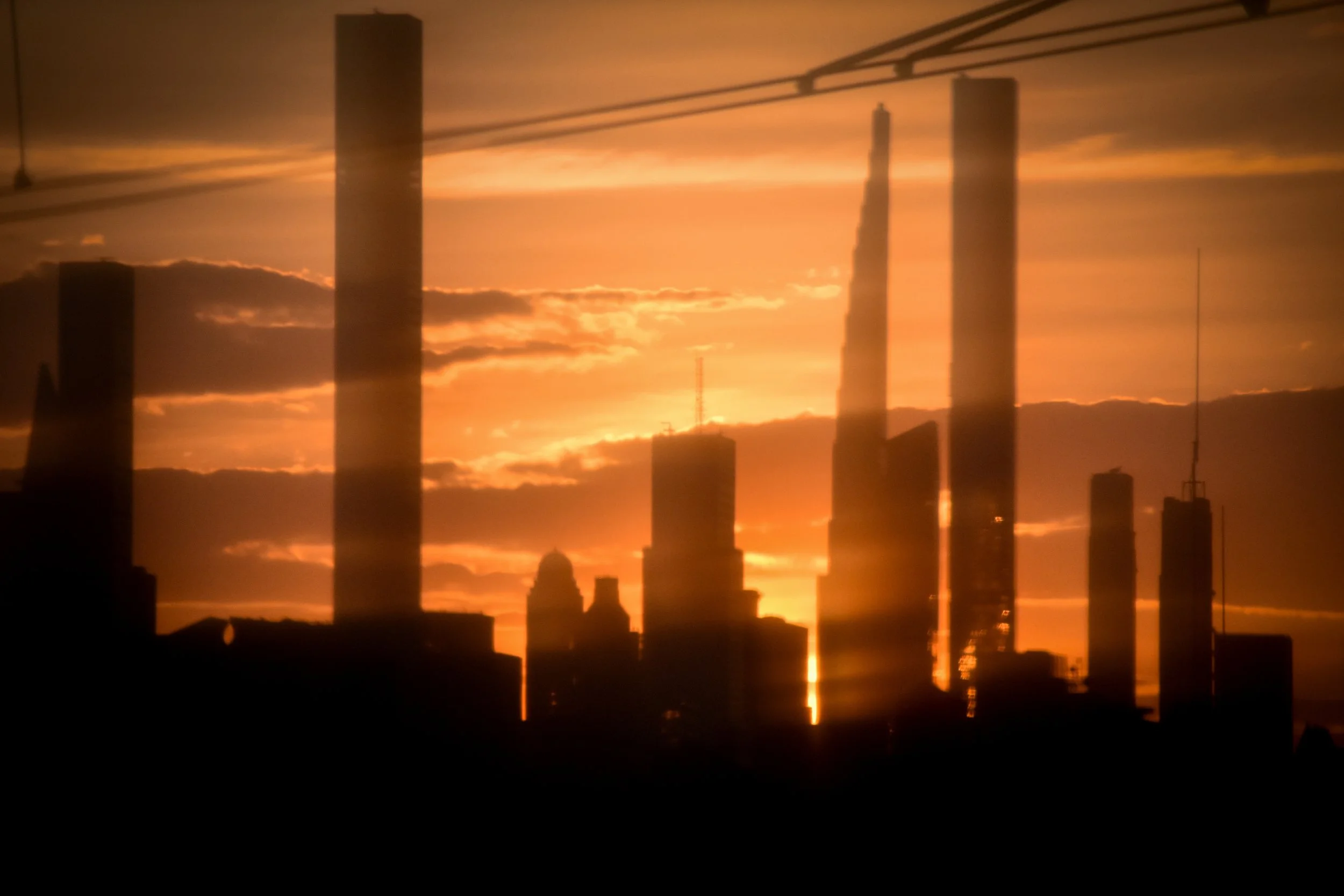 City skyline at sunset with tall buildings and reflections on water.