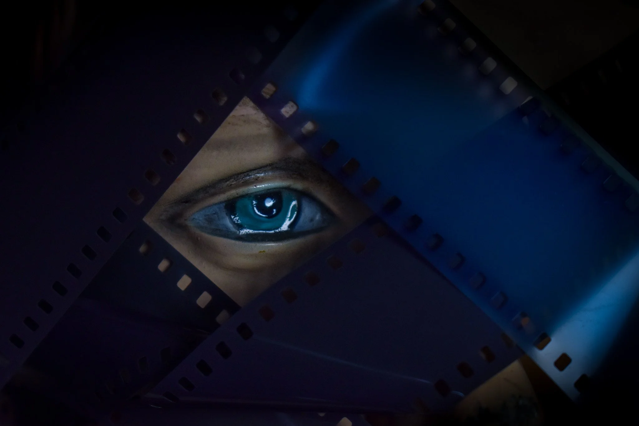 Close-up of a printed eye illustration with blue sclera, black pupil, and detailed iris, inside a dark frame or holder with perforations.