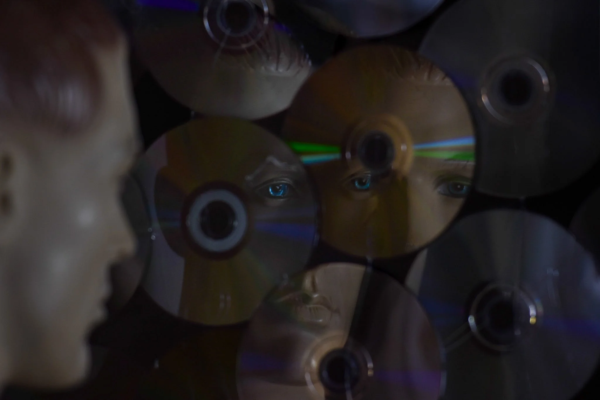 A collection of CDs or DVDs stacked closely together with reflections and a dark background.