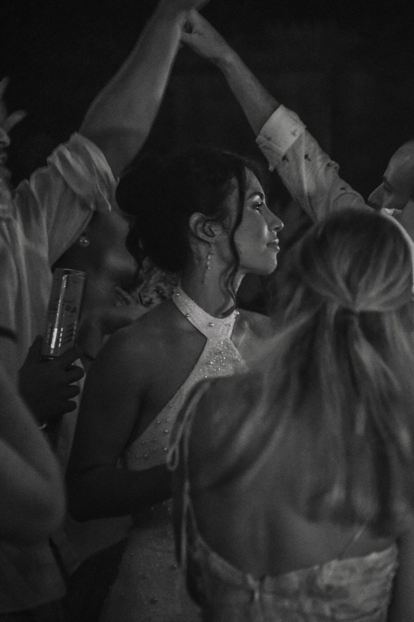 A black and white photo of a woman in a glamorous dress at a social event, with others around her, some holding drinks.