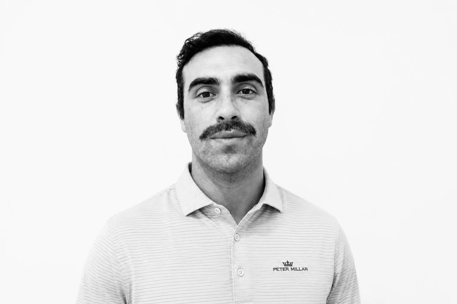 Matteo,founder, Rêverie Golf team member wearing a white Peter Millar polo shirt, portrait on a white background.