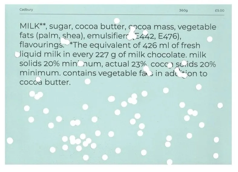 Close-up of the back of a Cadbury chocolate bar showing ingredients, including milk, sugar, cocoa butter, and vegetable fats, with white spots on the packaging.