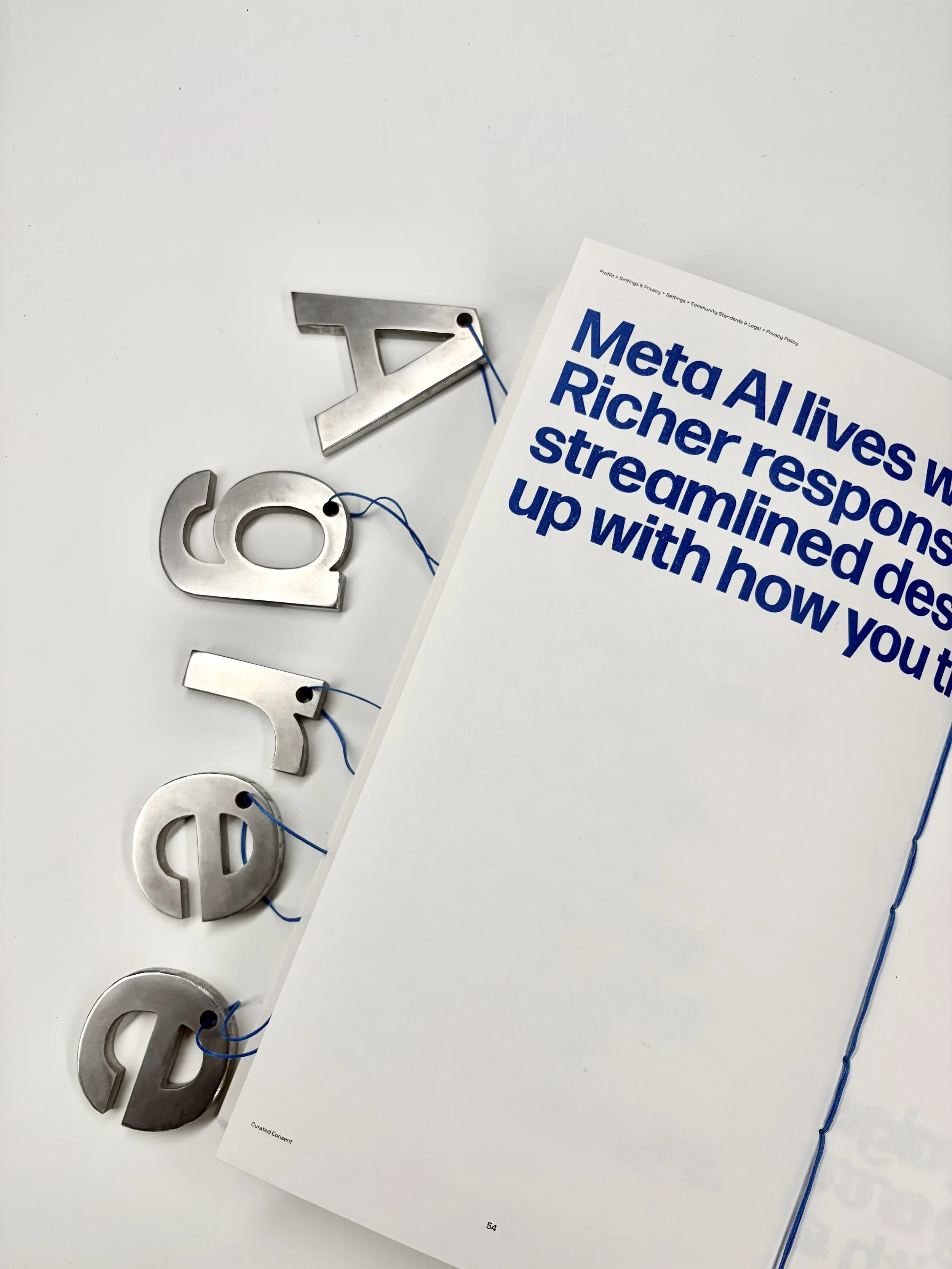 Metal numbers spelling out 'Agree on a white surface. Partially visible book page with bold blue text.