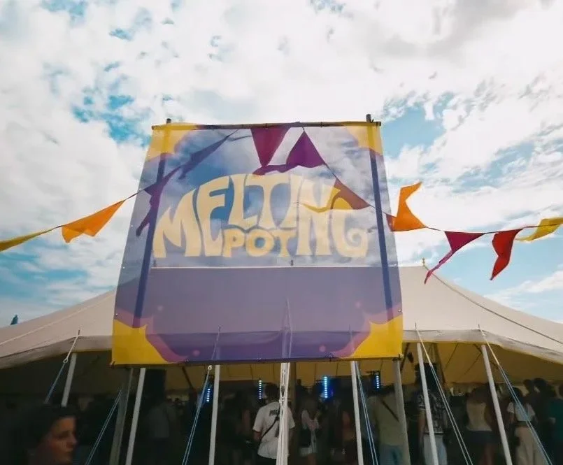 Carnival or festival tent with a large colorful banner and stringed flags, under a partly cloudy sky.