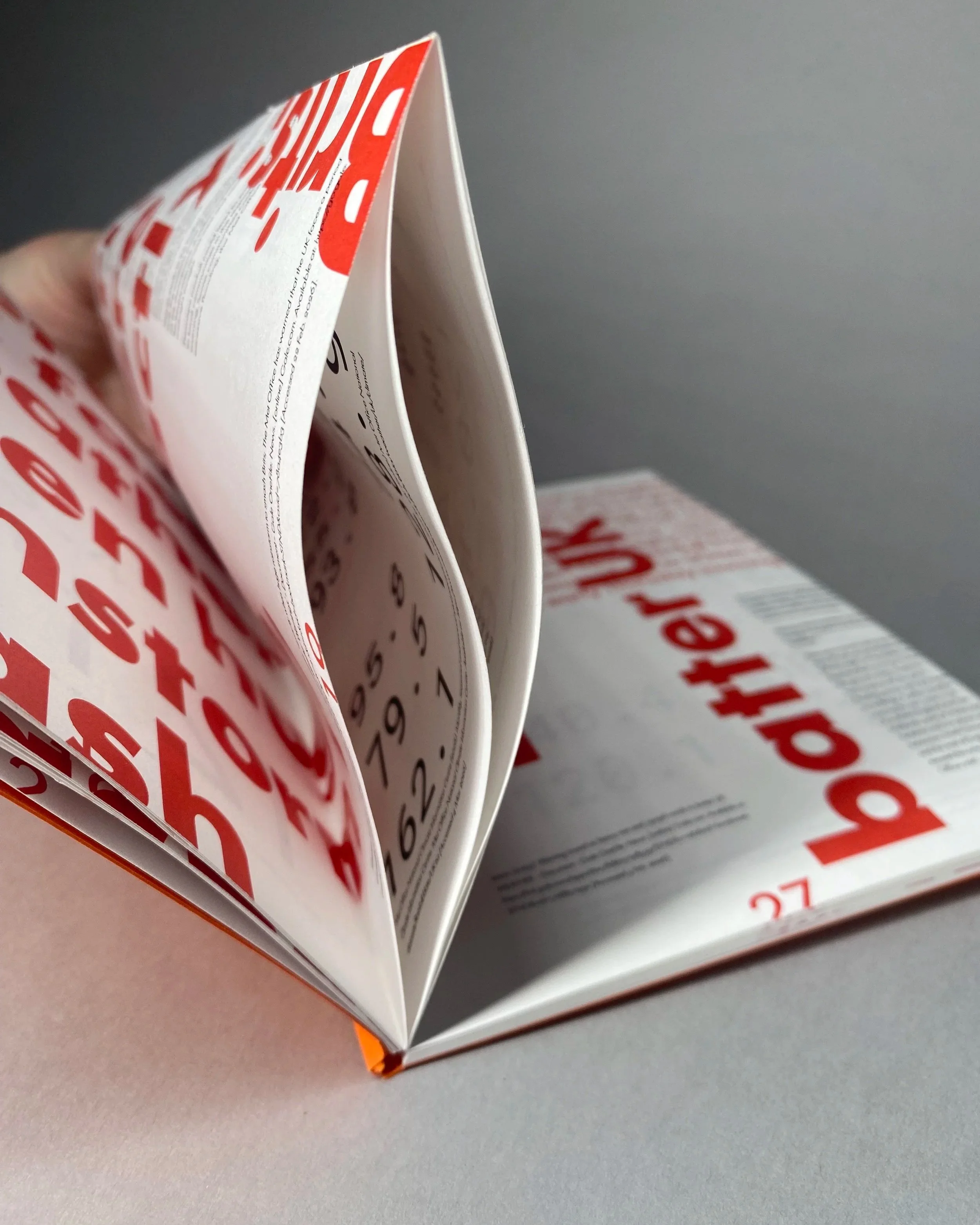 French folded pages in a book with bright orange text and smaller text hidden in the folds.