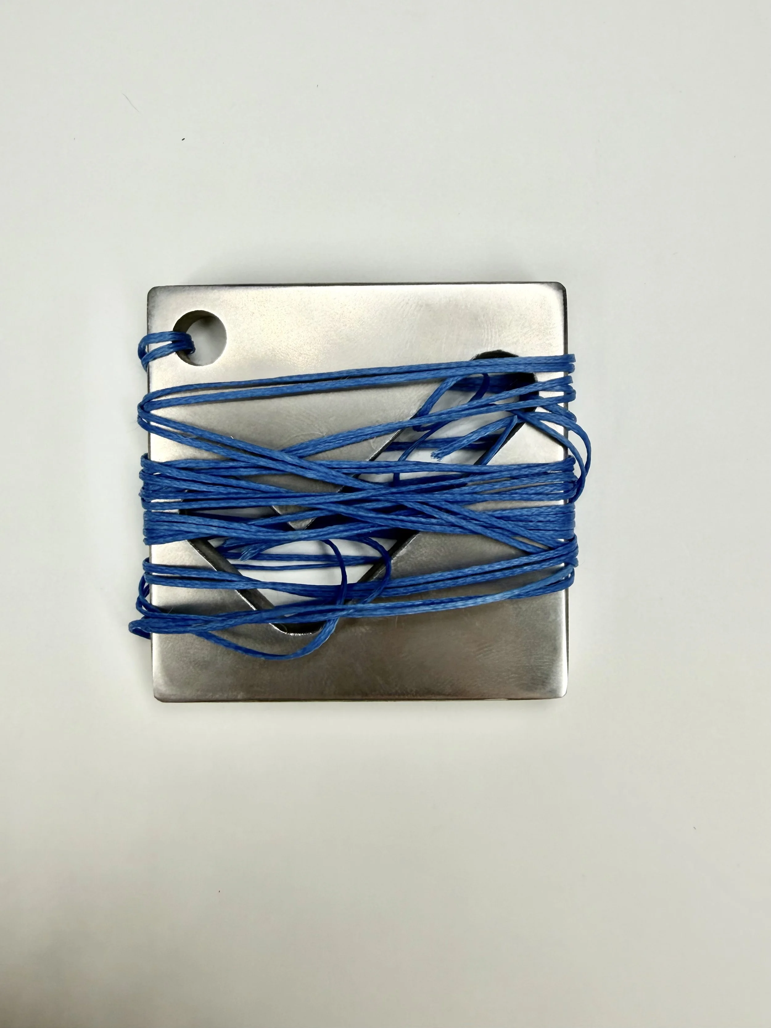 A silver metal weight attached to a blue string, which is wrapped around it multiple times, resting on a white surface.