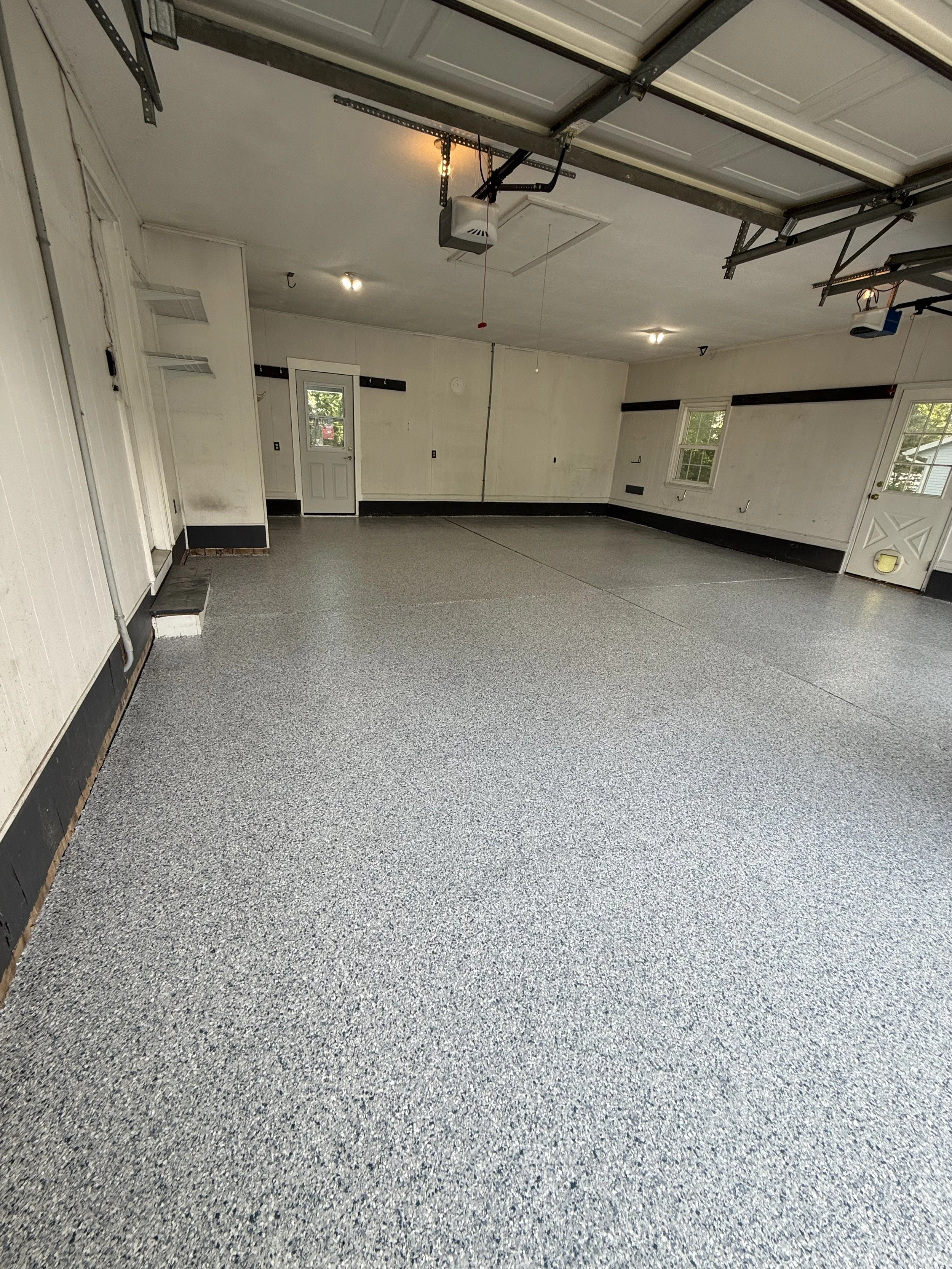 Empty garage with a speckled gray epoxy floor, white walls, and a partially opened garage door.