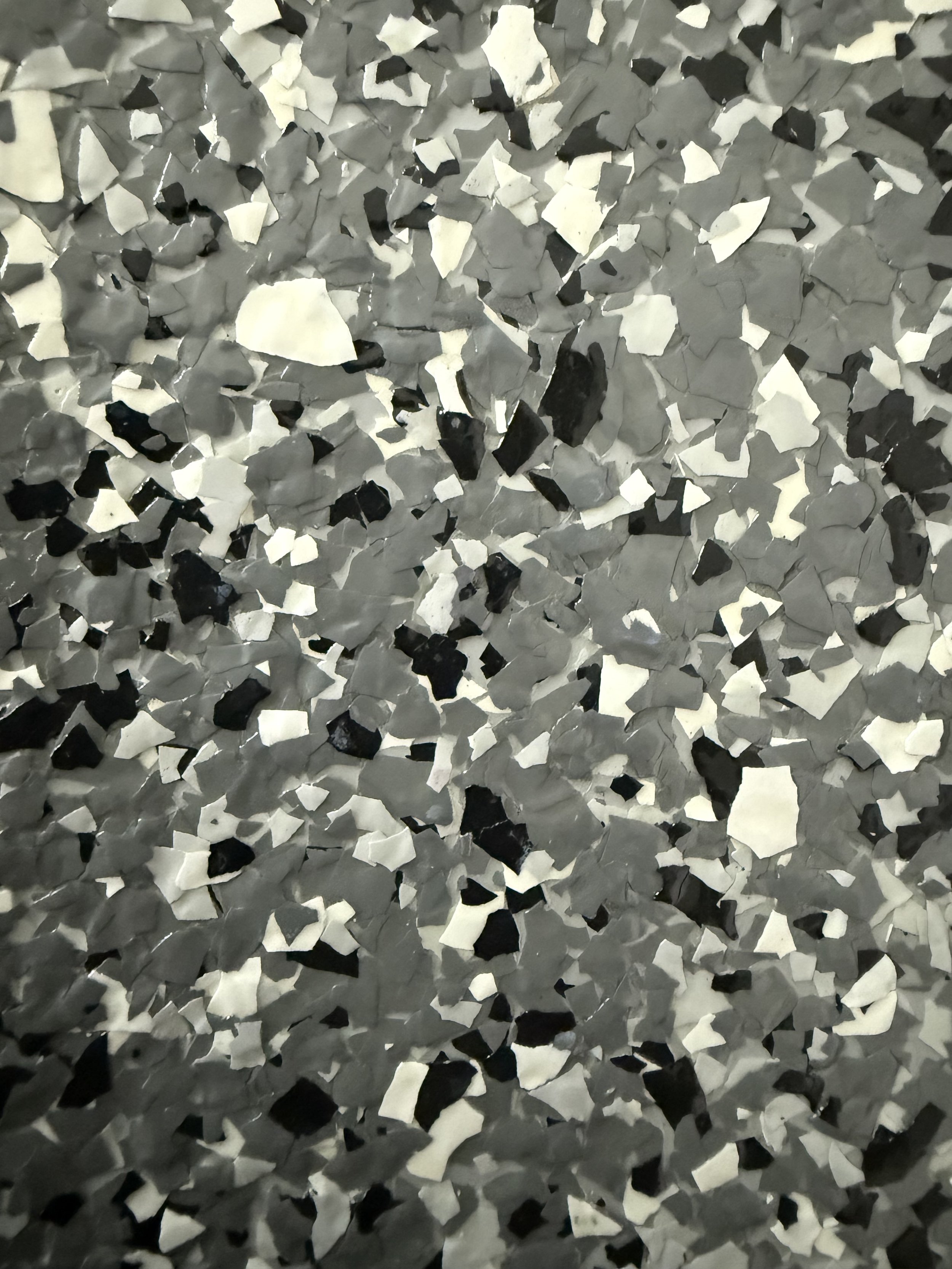 Close-up of a textured surface with small, irregular black, white, and gray snippets resembling a mosaic or terrazzo pattern.
