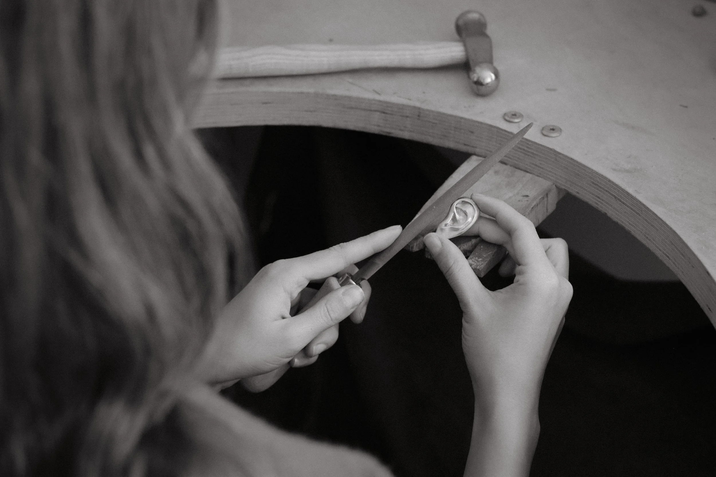 Jeweller works on ear-shaped pendant at jewellery bench