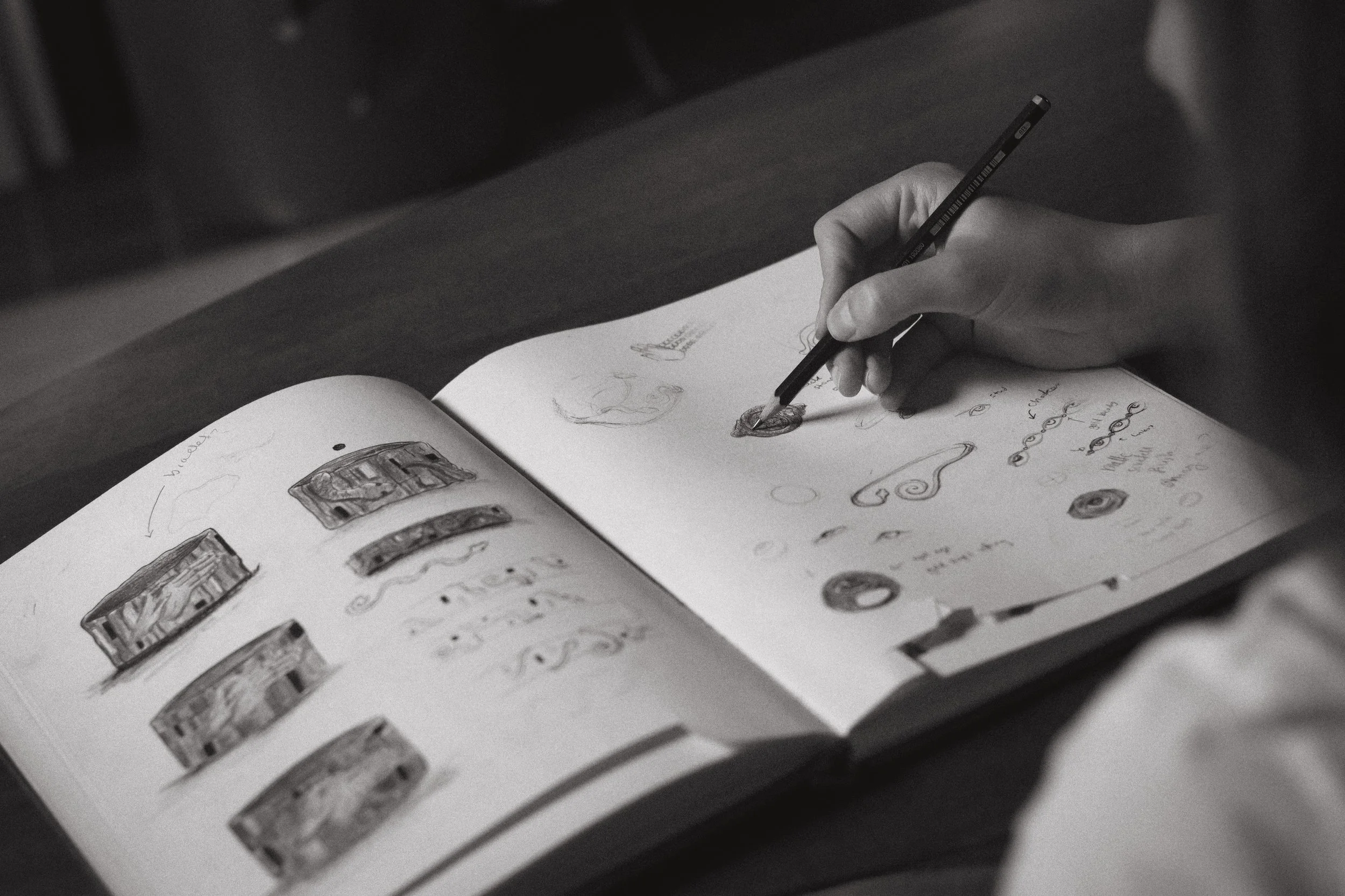 Jeweller sketching surreal jewellery illustrations in a notebook with a pencil.