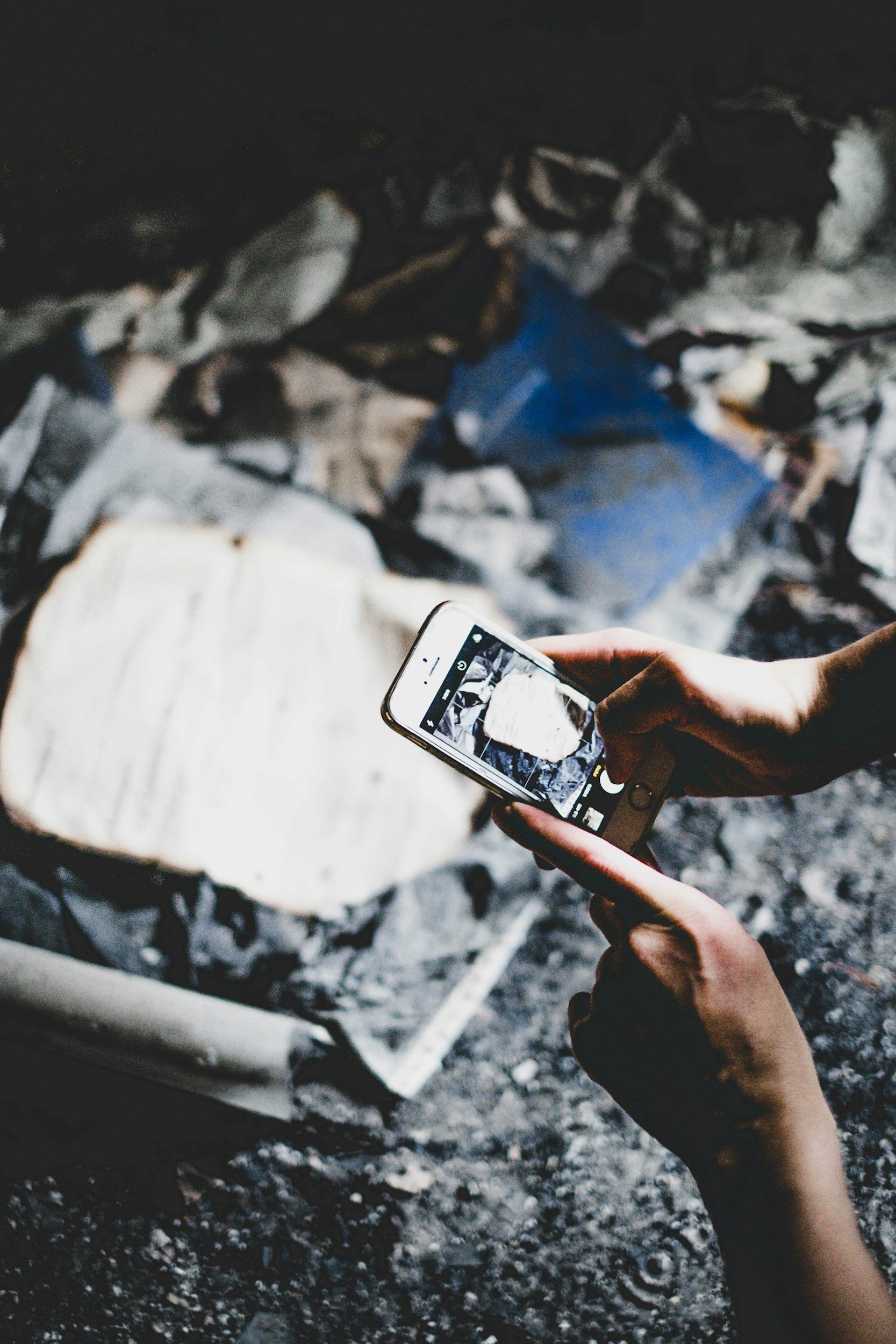 Person holding a smartphone taking a photo of a charred fireplace filled with ashes and debris.