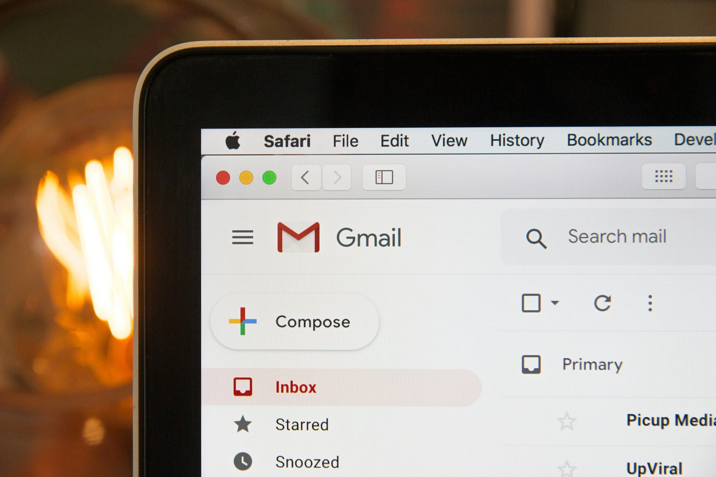 Close-up of a laptop screen displaying a Gmail inbox with the menu bar visible, showing options like Compose, Inbox, Starred, Snoozed, and UpViral, against a blurred background.