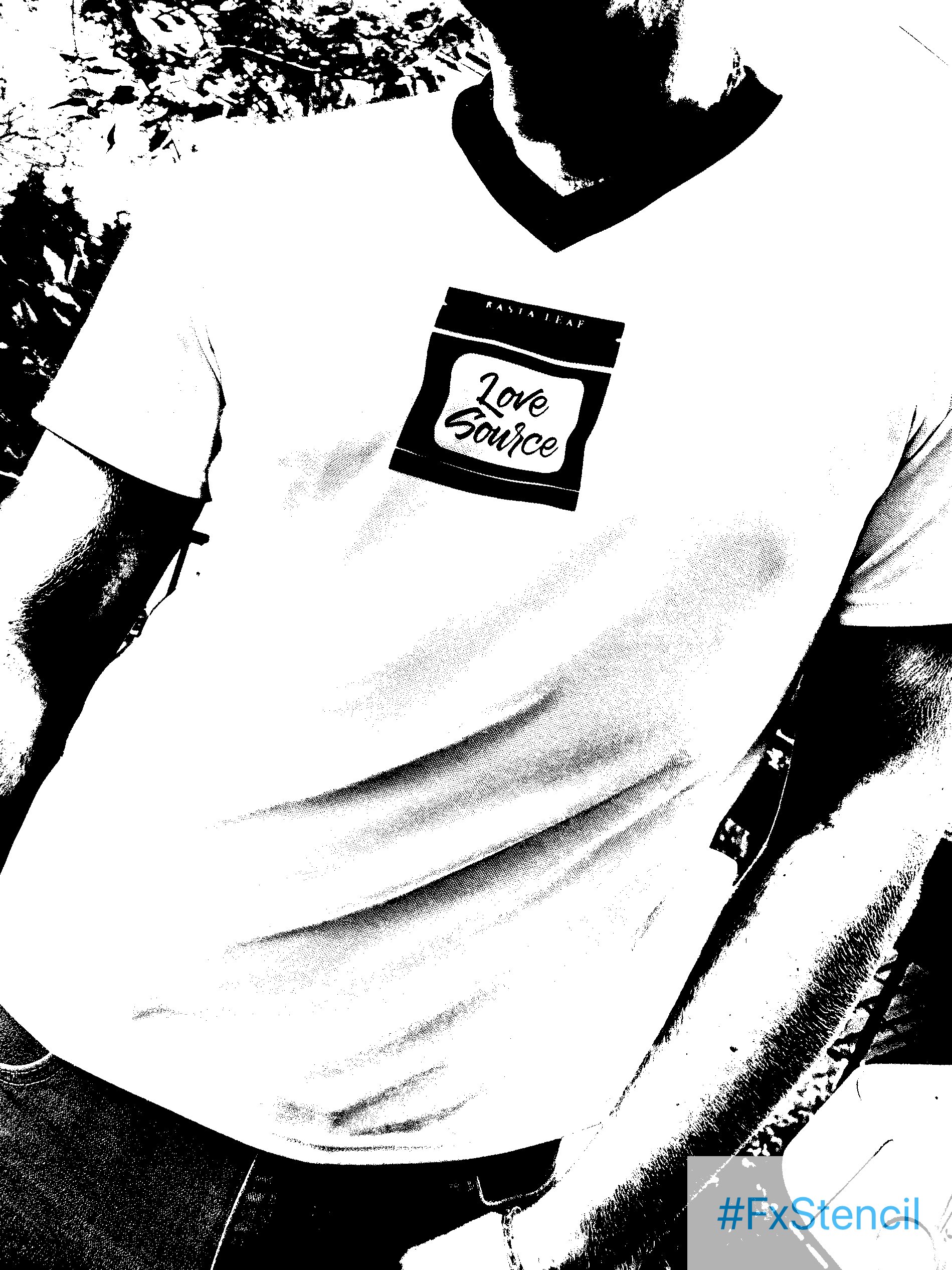 Close-up of a person wearing a white T-shirt with a label, styled like a bag of tobacco, that says 'Love Source' and some greenery in the background, black and white photo.