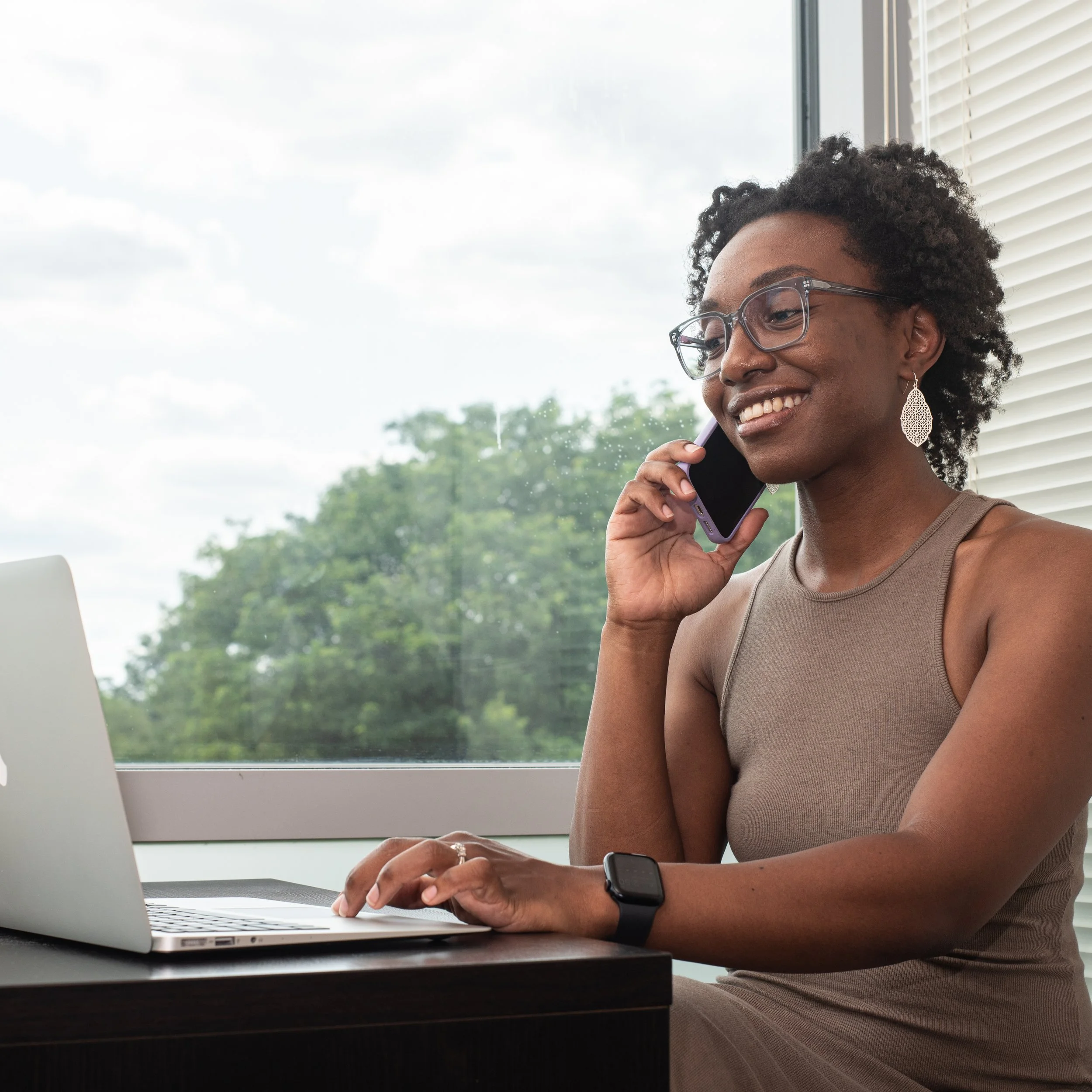 Wellness coach Rebecca Danae Cortes smiling while taking a call and working on her laptop.