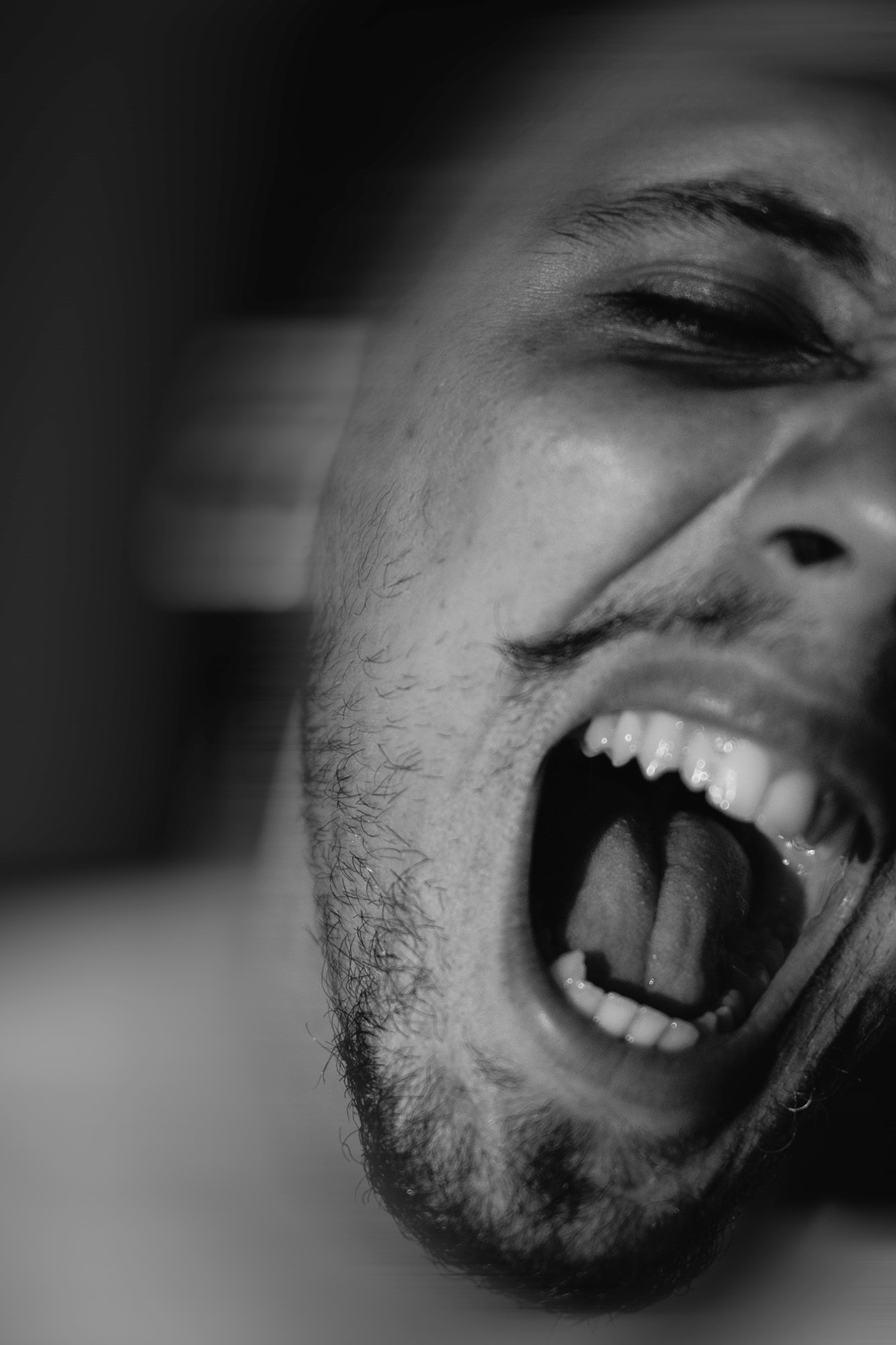 Close-up de um homem sorrindo com a boca aberta, mostrando os dentes e a língua, em preto e branco.