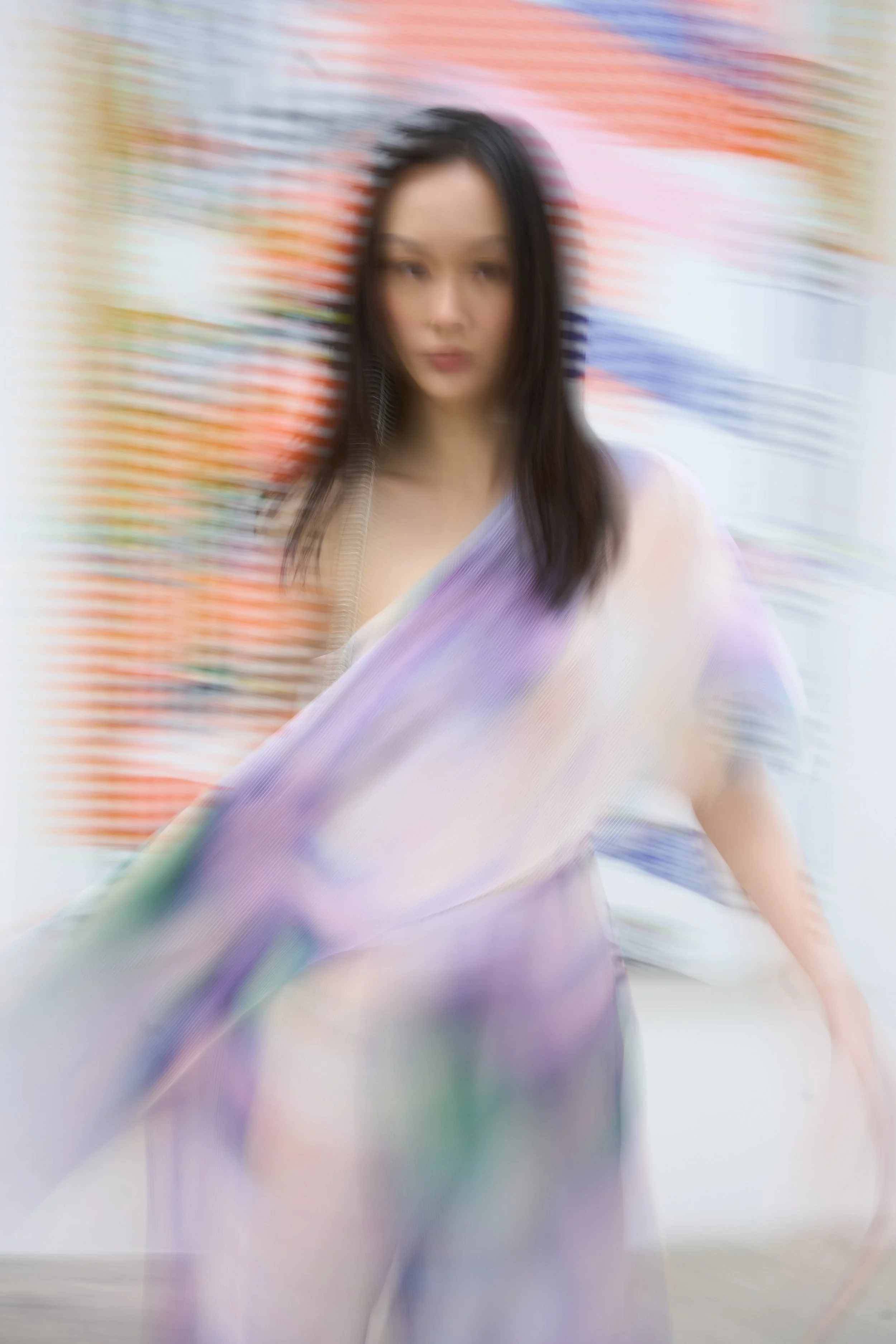 Blurred portrait of a woman with dark hair wearing a colorful shawl, with a vibrant colorful background.
