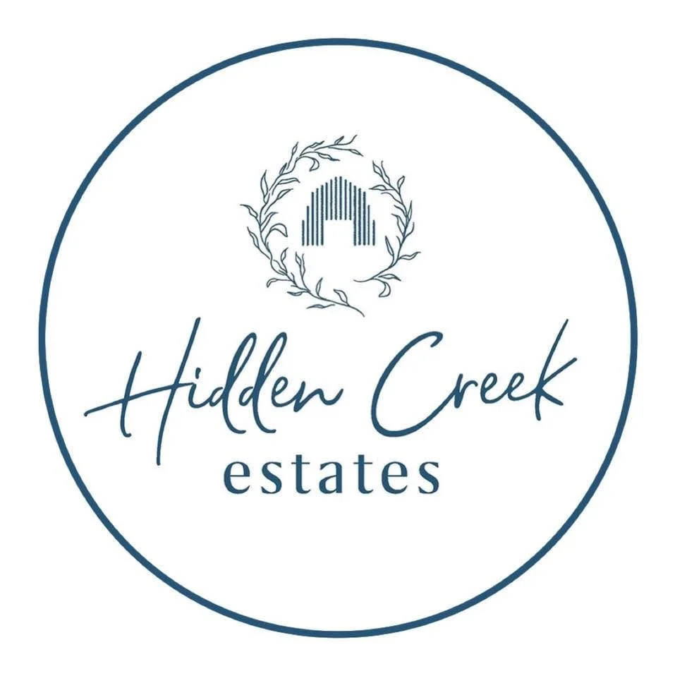 Logo for Hidden Creek Estates with a circular border, a stylized 'A' surrounded by leaves at the top, and the name in scripted and serif fonts.