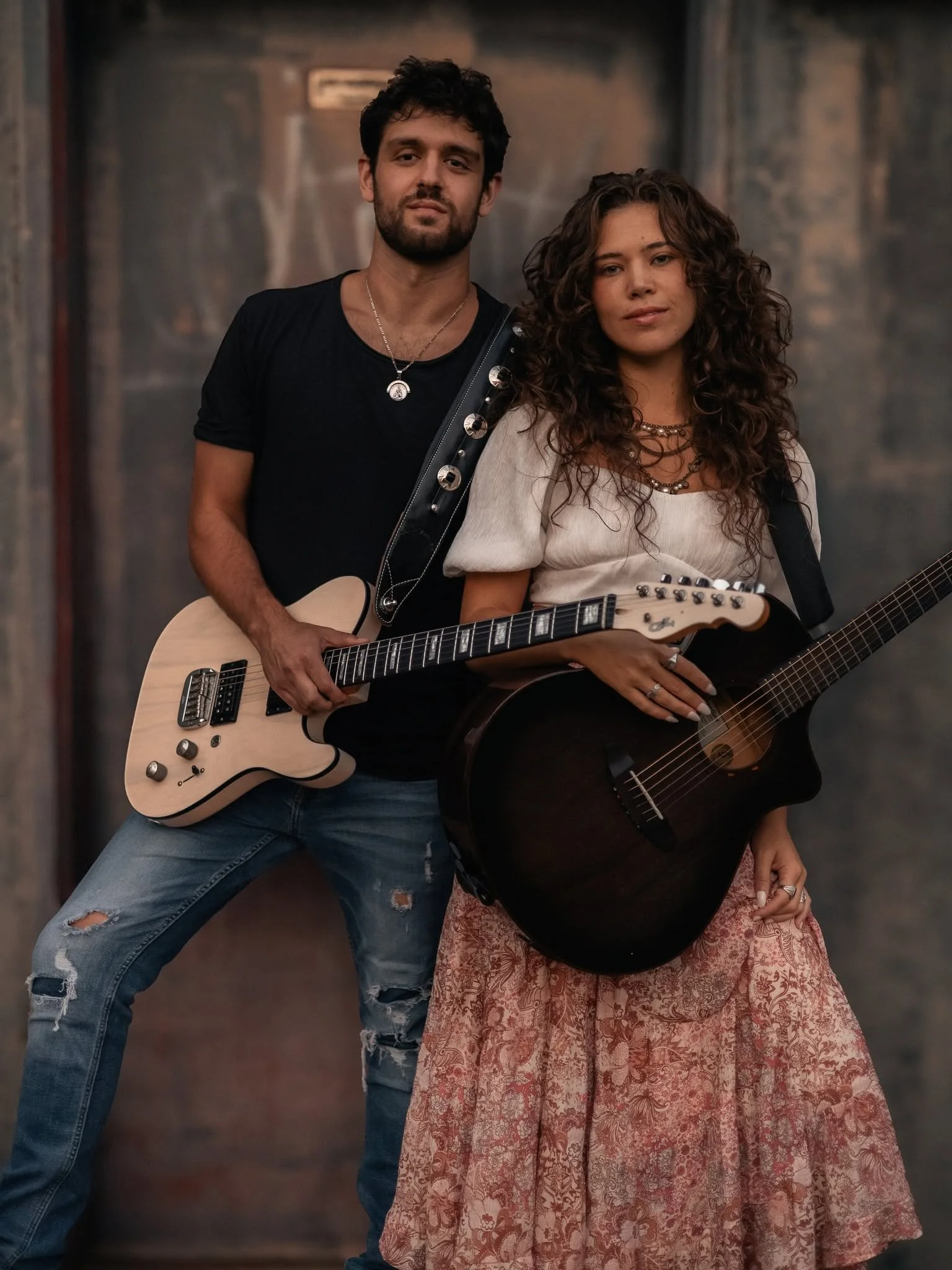 A man and a woman holding guitars, standing together in an indoor setting.