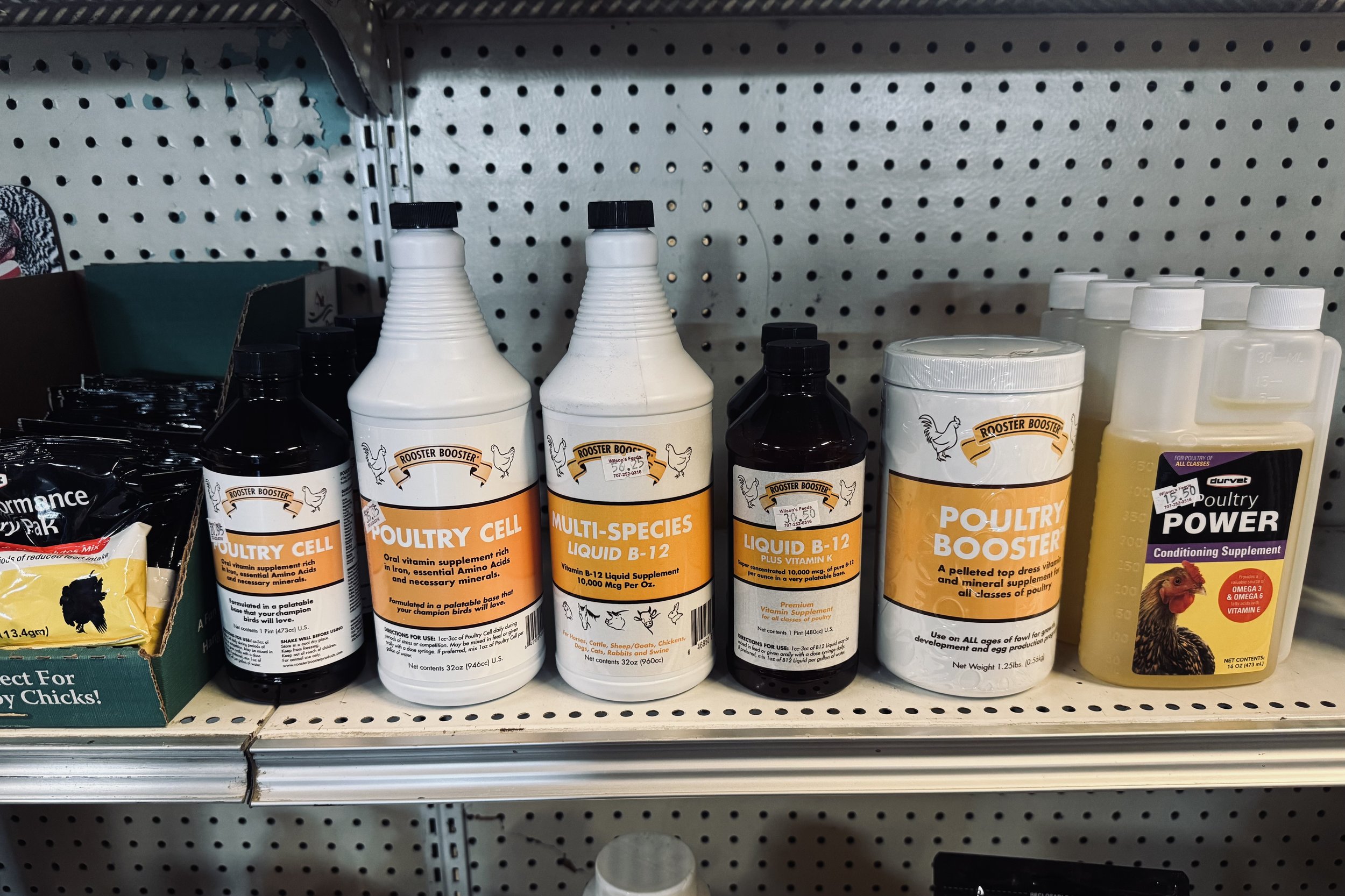 Shelf with poultry supplements including bottles labeled 'Poultry Cell,' 'Multi-Species Liquid B-12,' 'Poultry Booster,' and 'Poultry Power' in a store.