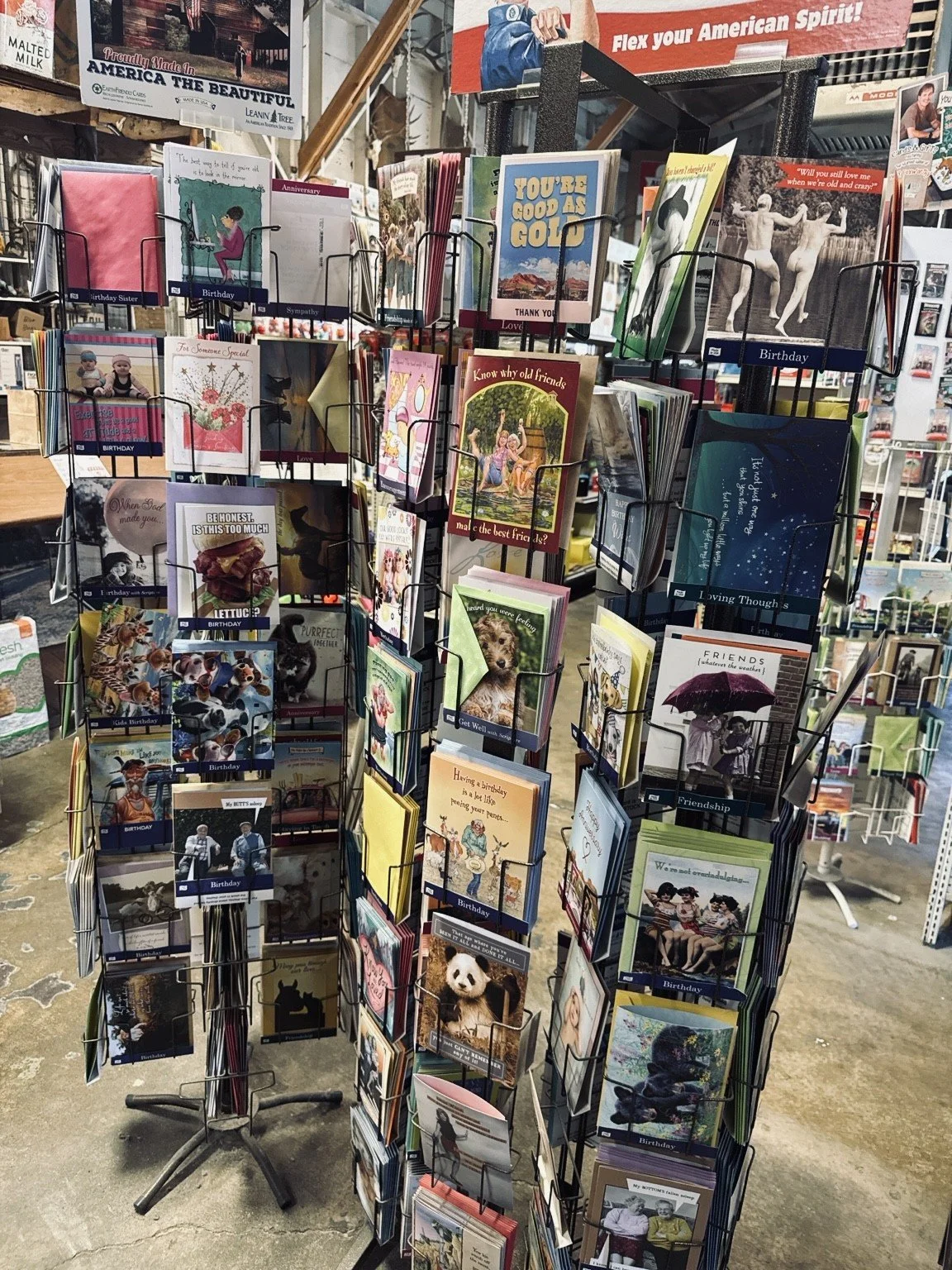 Display rack of greeting cards featuring various designs and messages, with shelves and signs in a store environment.
