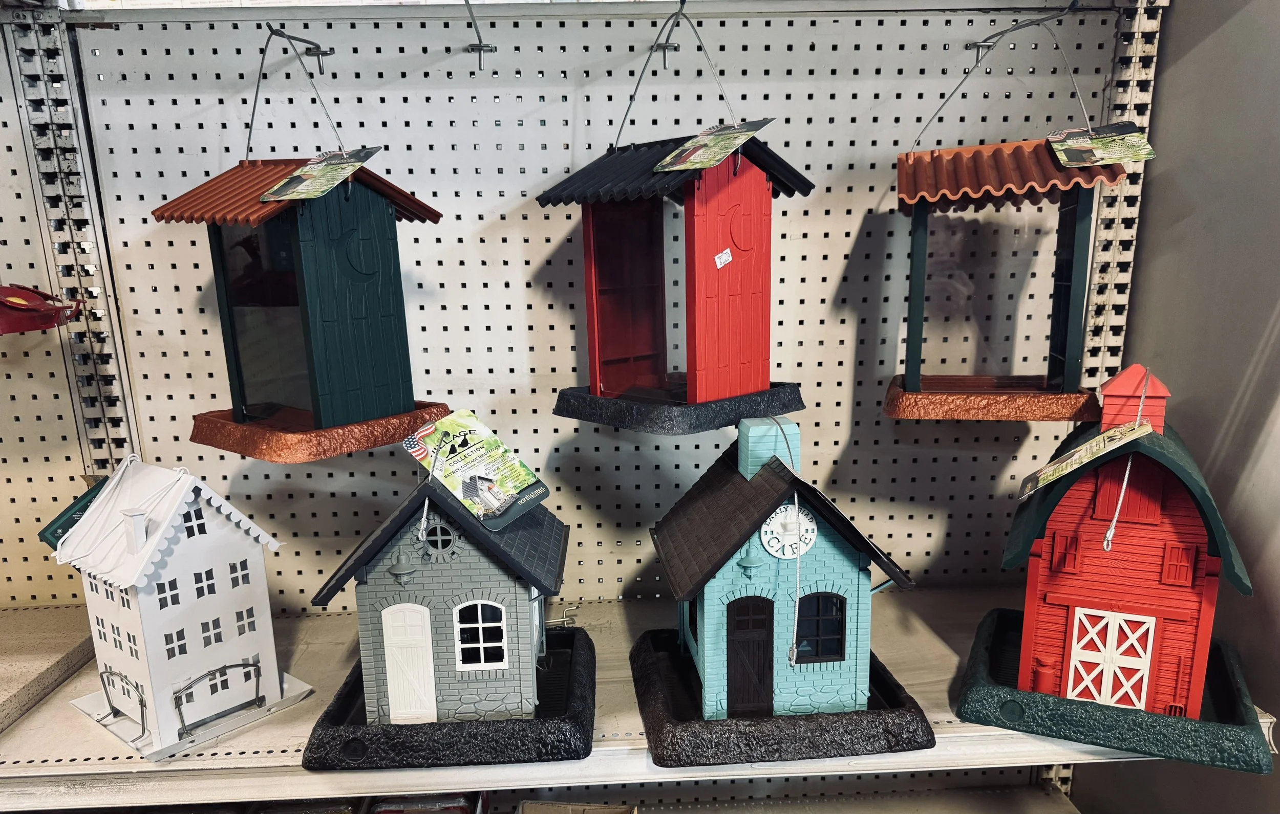 Various decorative birdhouses on store shelves, including a white house with cutout windows, a gray house with a gable roof, a red barn-style house, and others with different roof styles and colors.