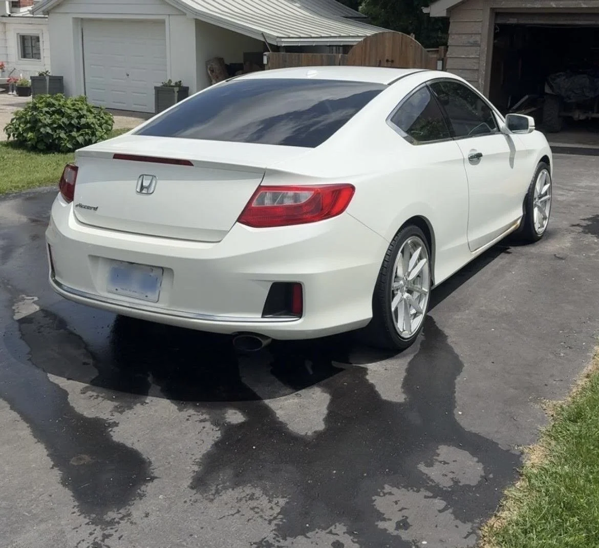 White Honda Accord coupe parked on a driveway with wet patches and grass on the side, with a garage and backyard in the background.