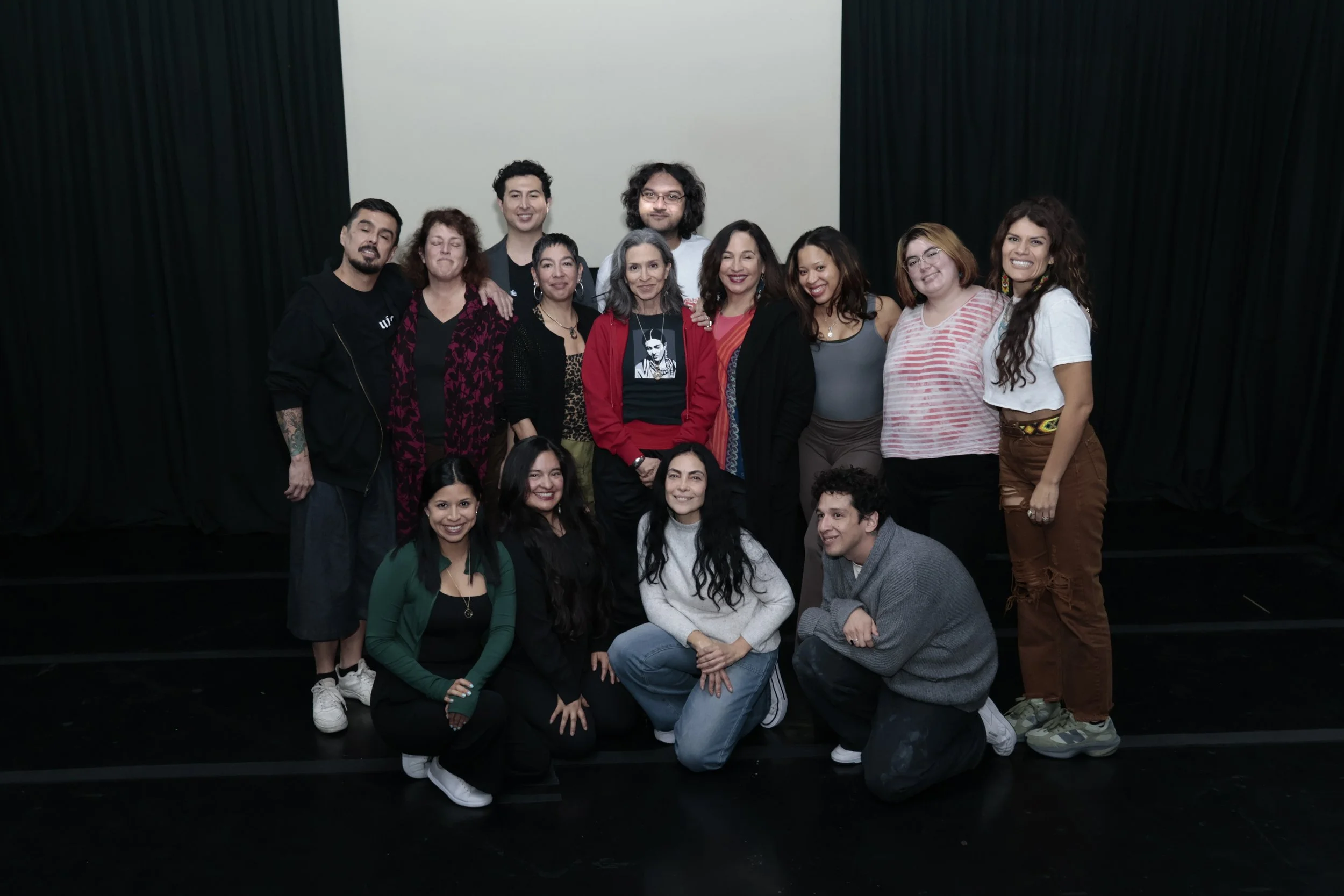 Group of diverse people smiling and posing together on a stage with a blank white screen behind them.