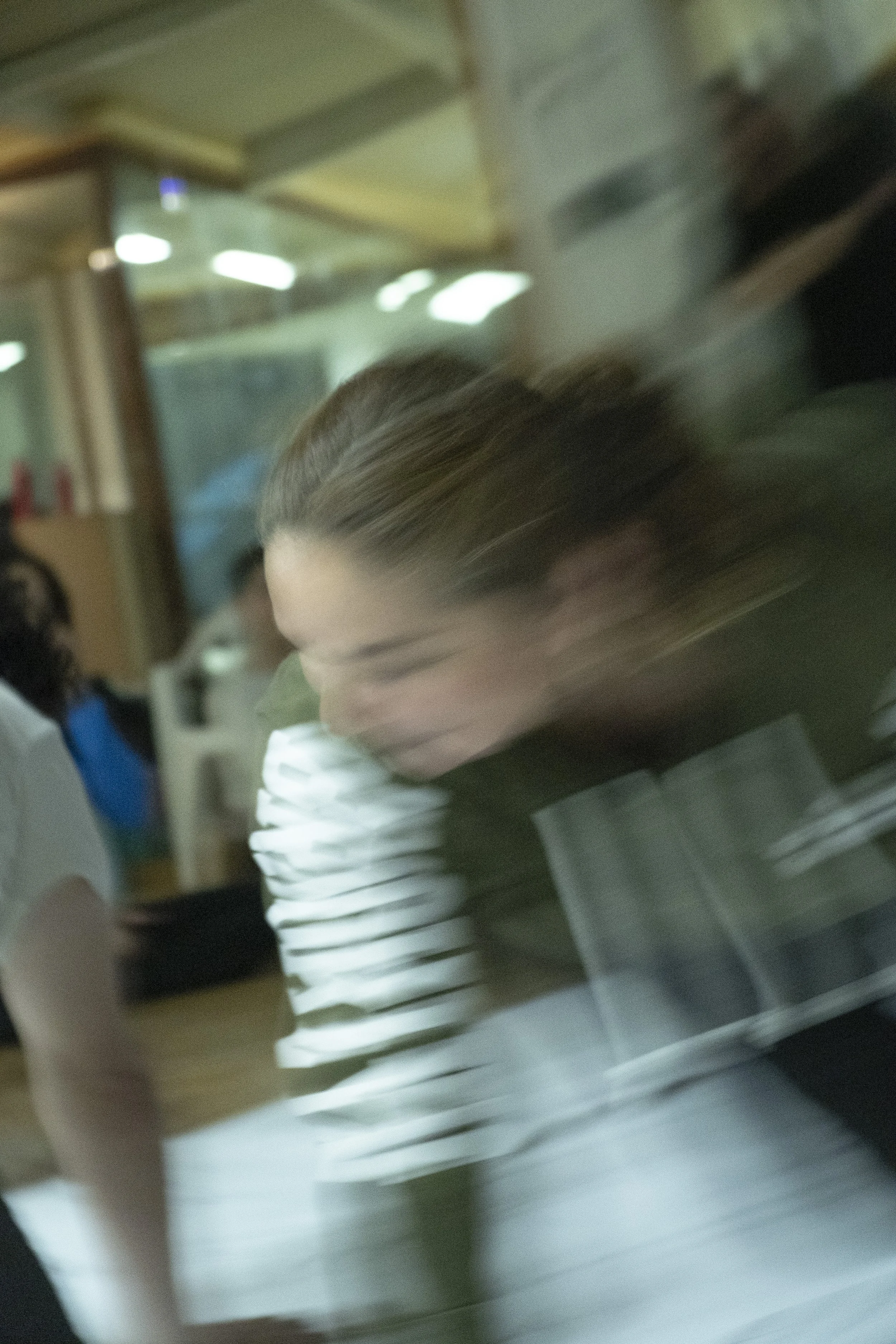 Blurred image of a woman with brown hair working on a laptop at a desk, with shelves and lights in the background. awaken your artist, casa hechale