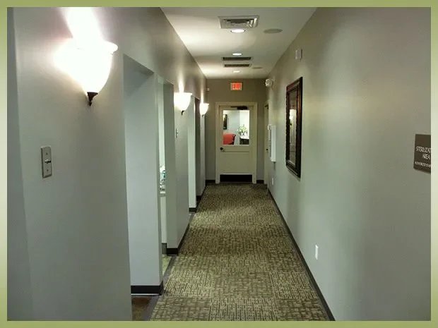 Empty hallway in a building with wall-mounted lights, framed picture, and a door at the far end.