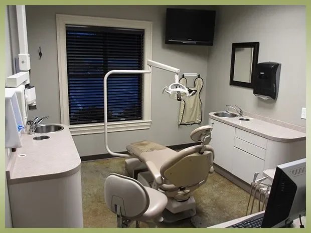 Dental examination room with a dental chair, equipment, window, TV, and sink.