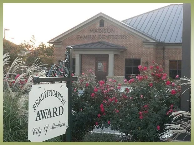 A brick building with a sign that reads 'Madison Family Dentistry' and a garden with pink flowers in front.