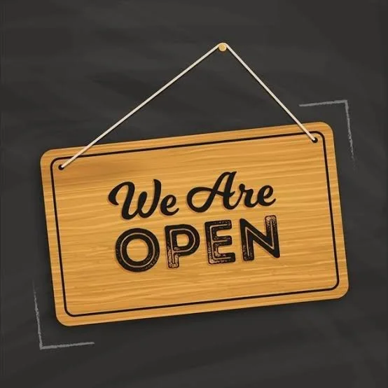 Wooden sign hanging with a string, displaying 'We Are OPEN' in black text on a dark background.