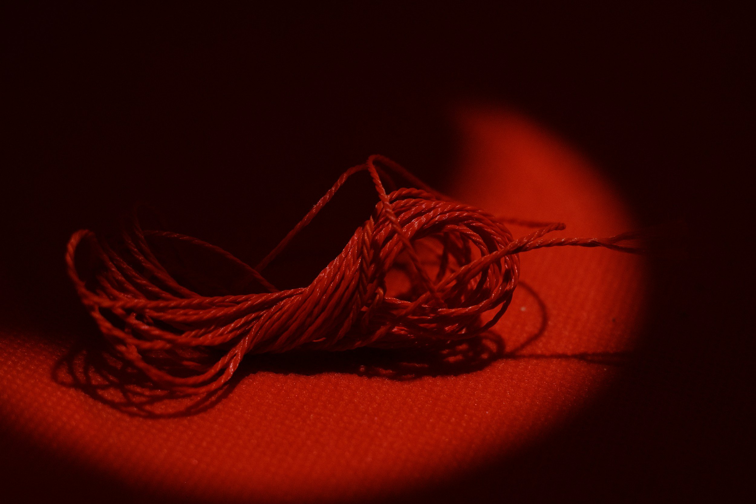 Red thread tangled on a red surface, dimly illuminated with a soft glow.