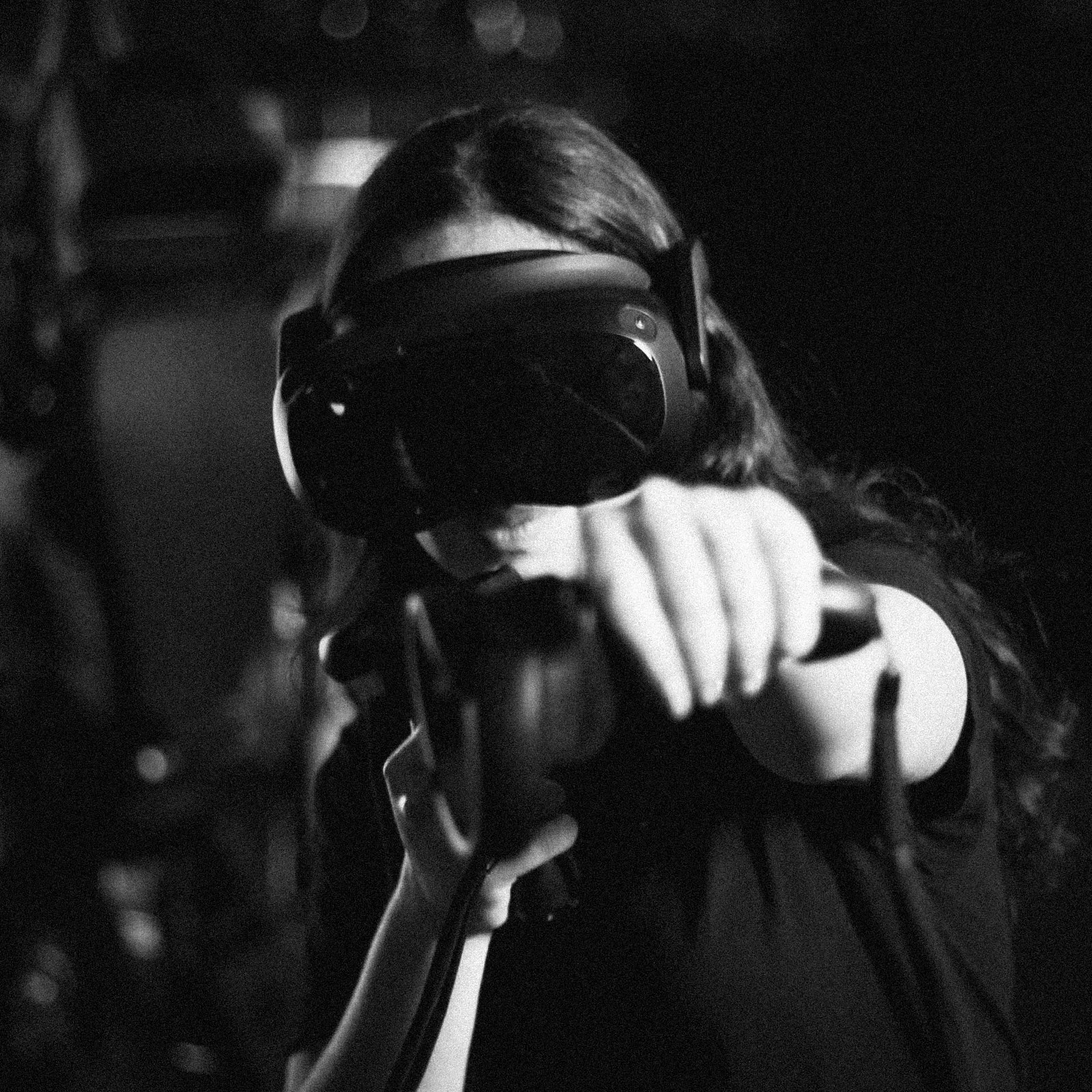 A person wearing a VR headset and a black t-shirt holding a VR controller, with a dark background.